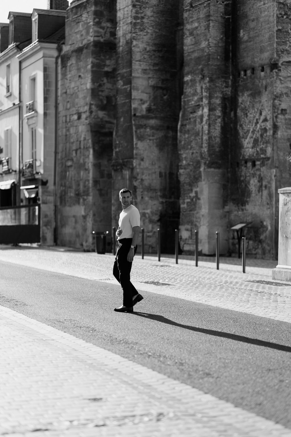 A sequence of black and white photos shows a person walking past stone columns casting dramatic shadows on a cobblestone street.