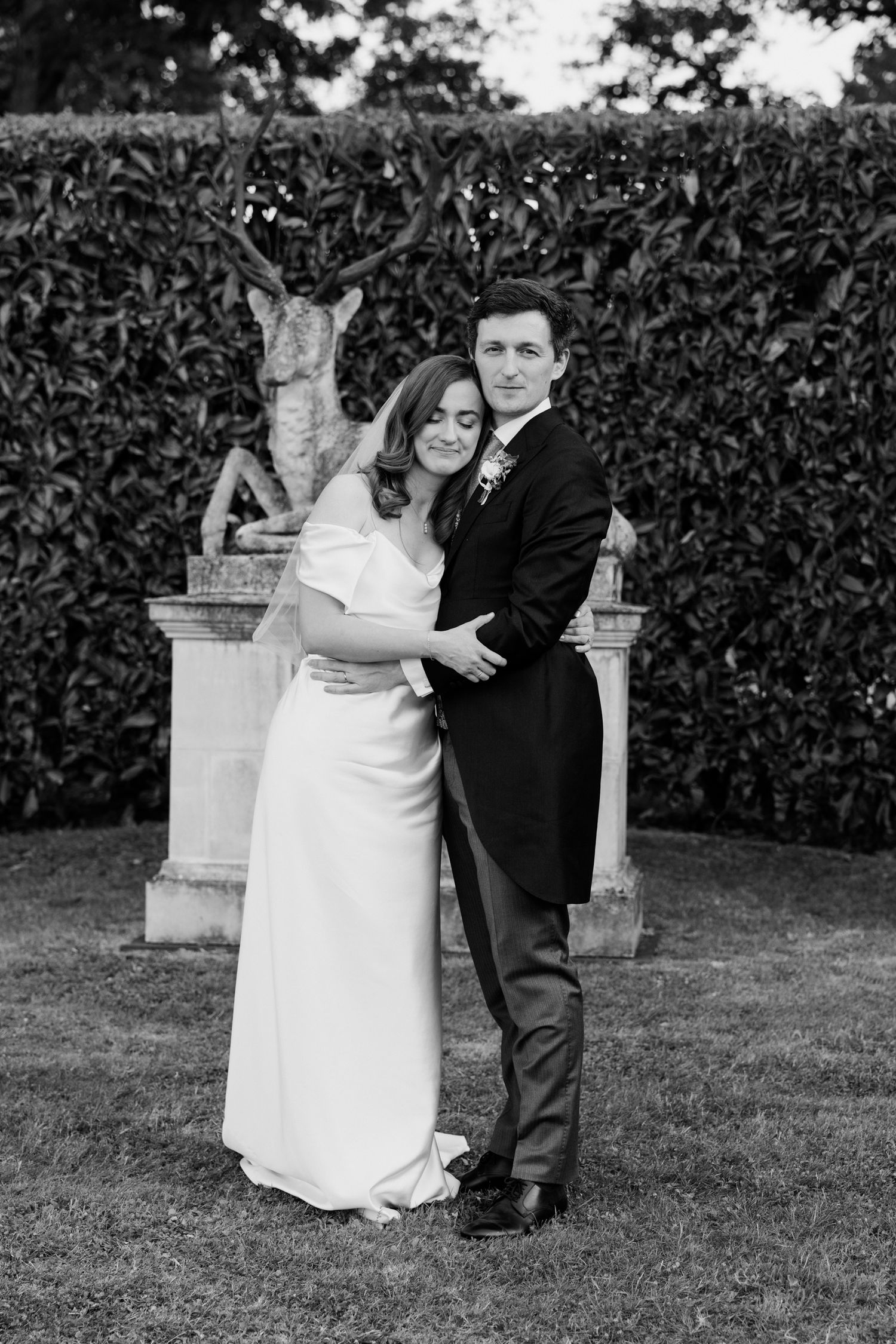 A couple in formal wedding attire shares an intimate moment in a garden setting in black and white photography. Luxury wedding france