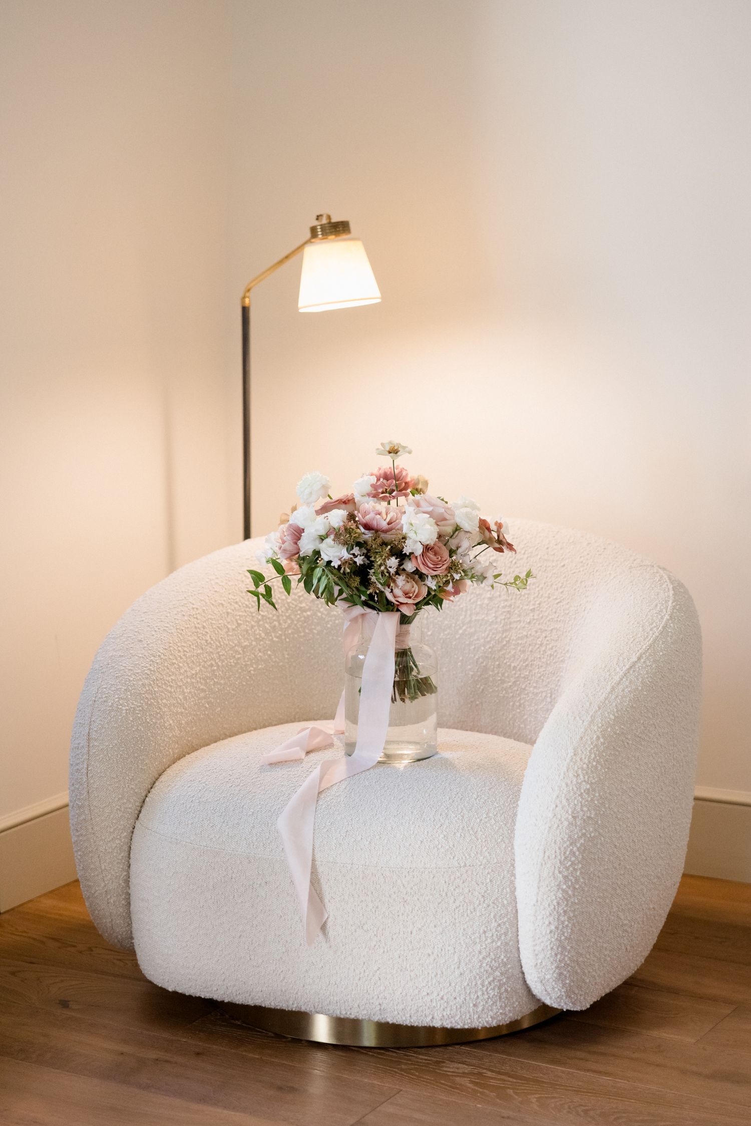 White curved modern sofa with plush boucle upholstery and floral arrangement on wooden floor in minimalist setting. Saint Remy de Provence