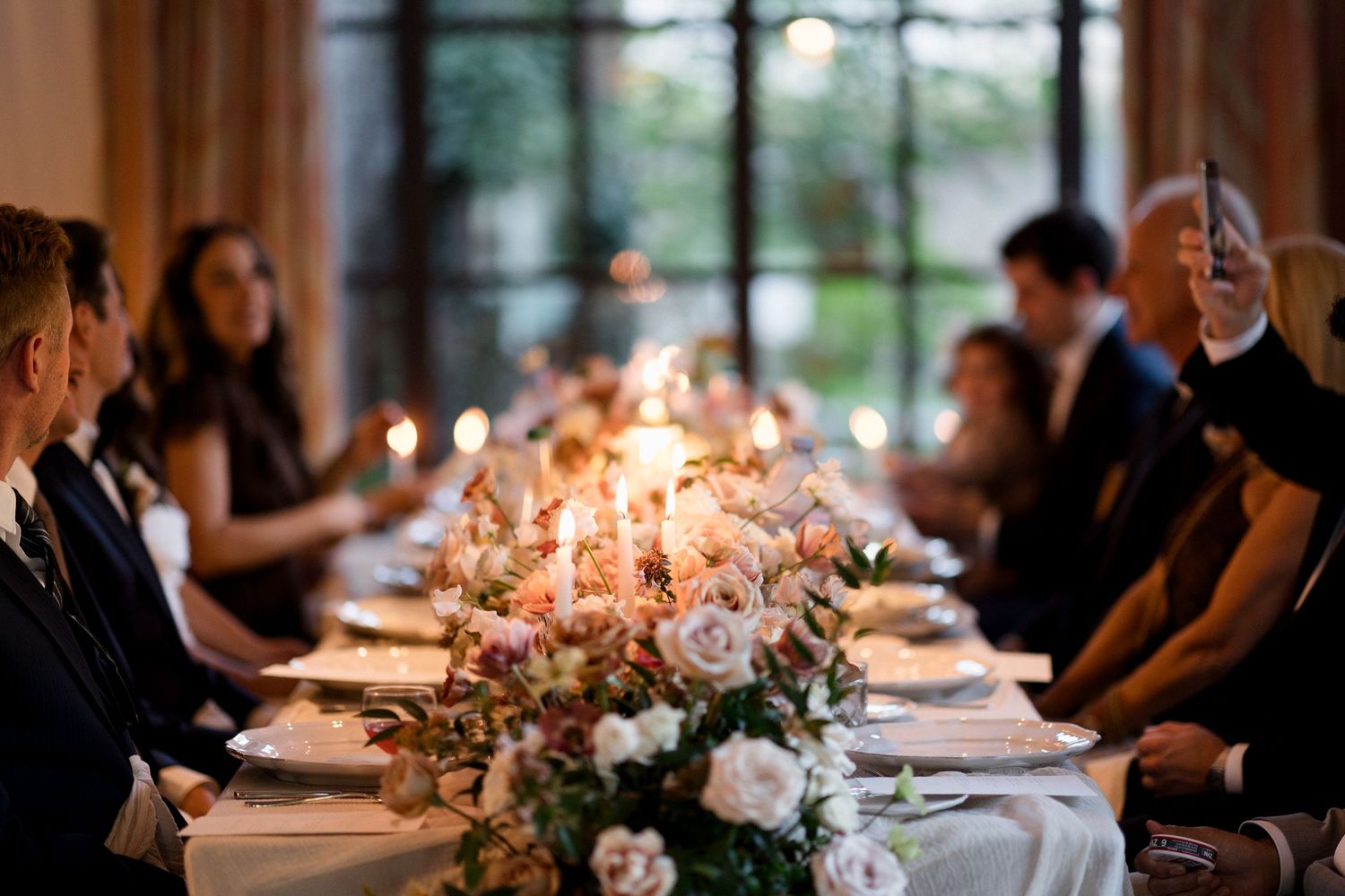 Elegant candlelit wedding reception tables decorated with floral centerpieces and glowing taper candles in a dimly lit venue.