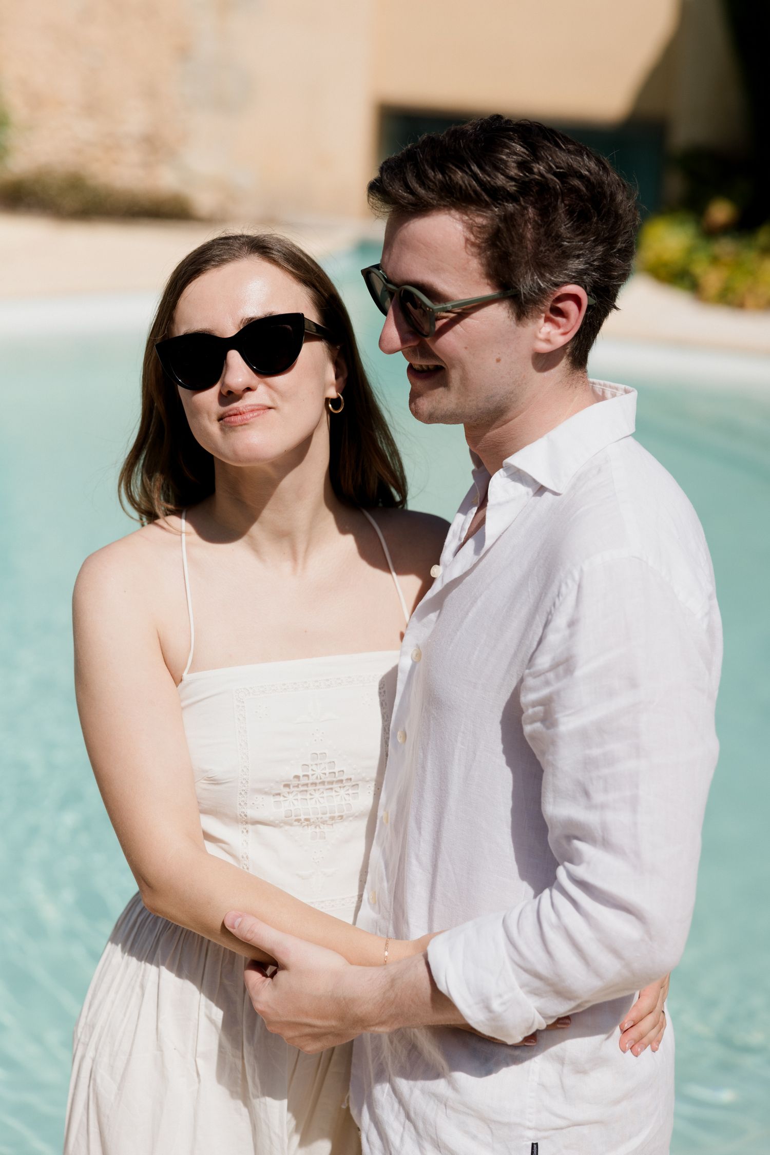 A couple in sunglasses and white outfits embrace by a pool on a sunny day.Brunch loire valley
