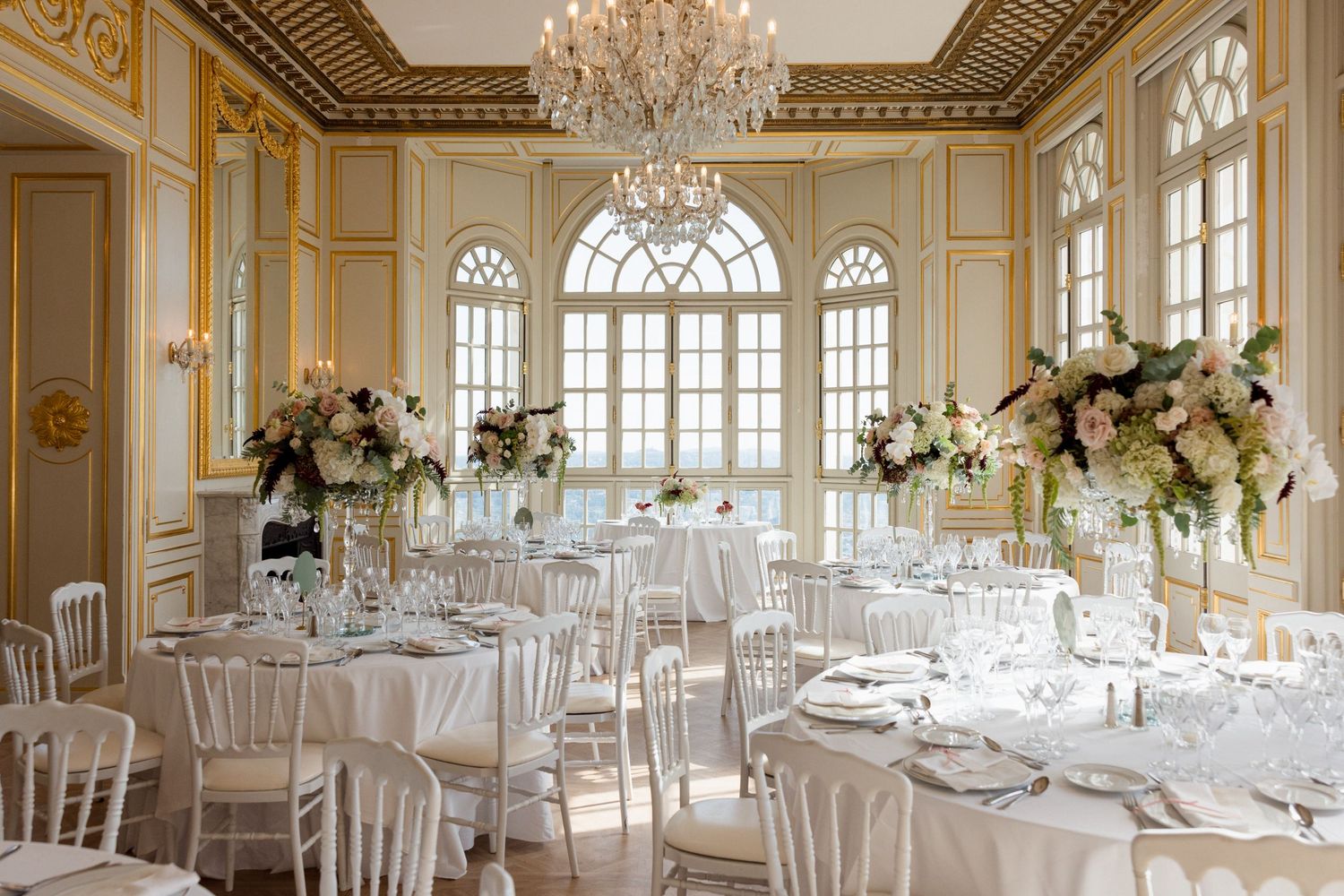 Elegant wedding reception setup in an ornate ballroom with crystal chandeliers and white-draped tables. destination wedding france Grasse