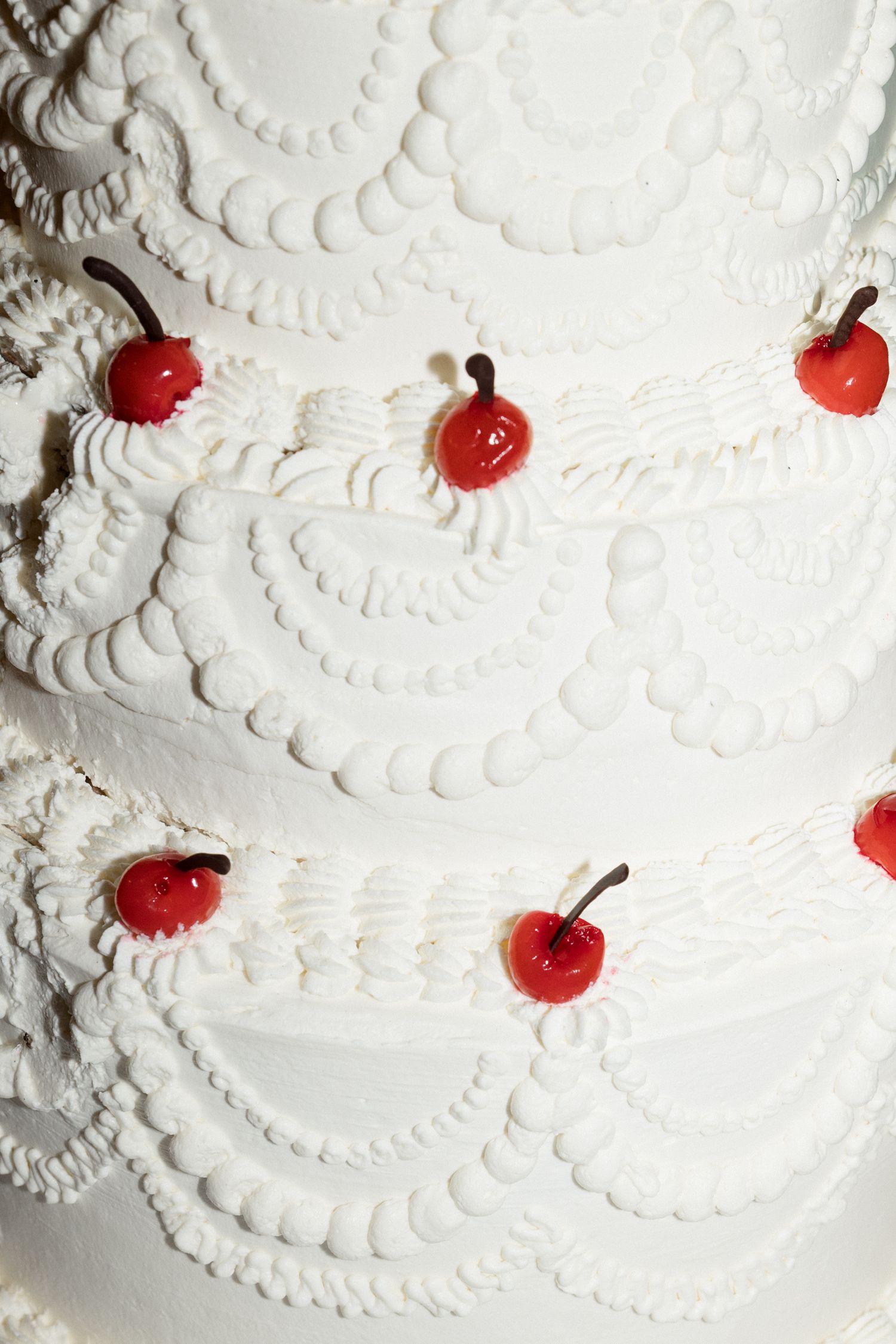 Close-up detail of white buttercream frosting with decorative swirls and small red cherry decorations on a cake. chateau saint georges