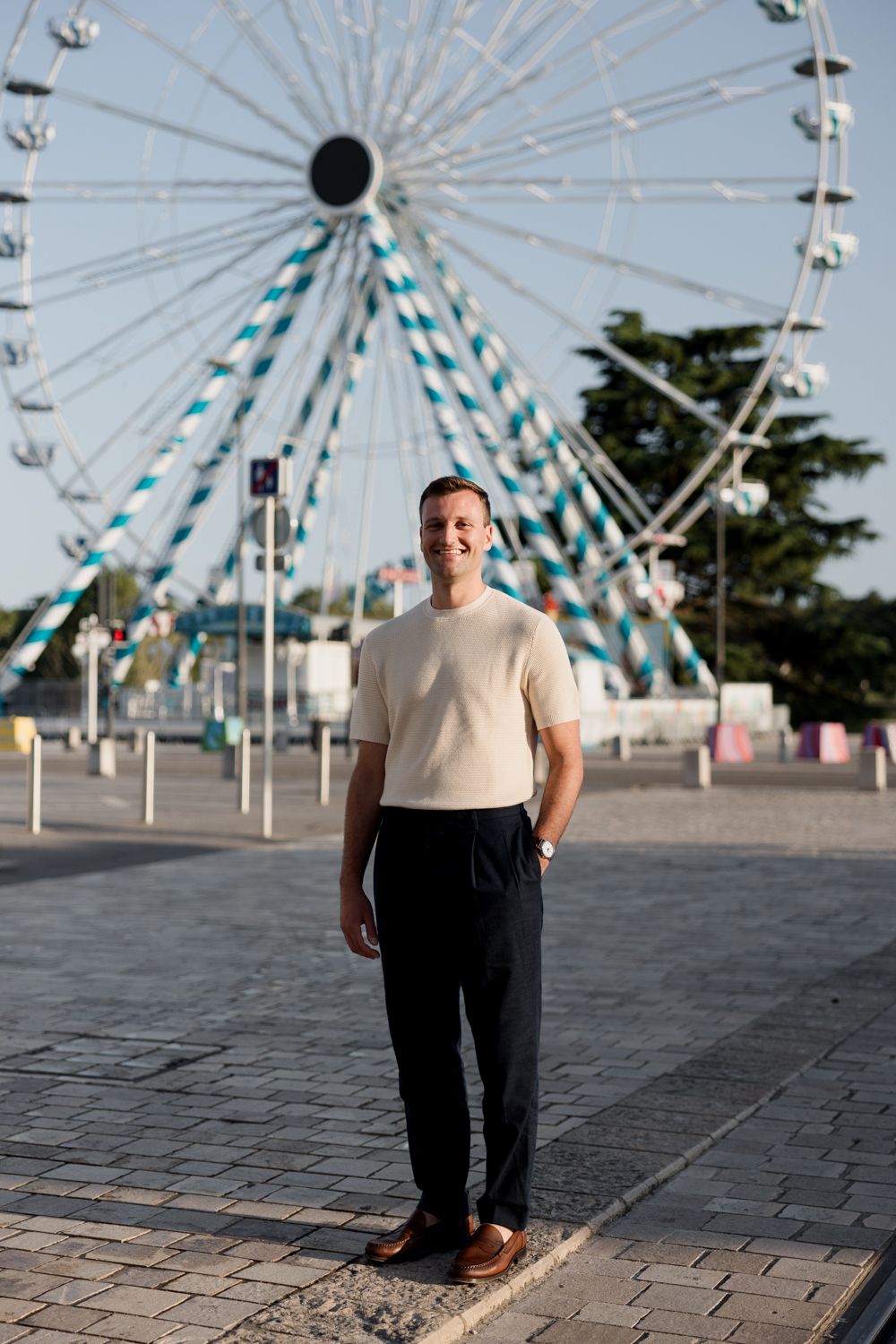 Couple standing together in front of a large ferris wheel on a paved plaza. Séance portrait Tours