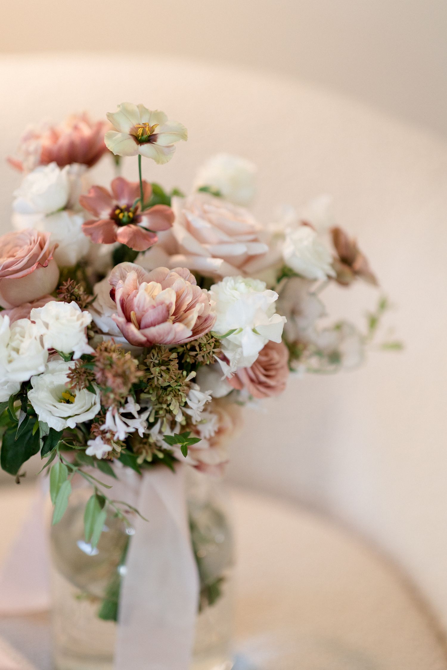 A delicate floral arrangement of blush pink roses and white flowers in a glass vase with a light ribbon accent.