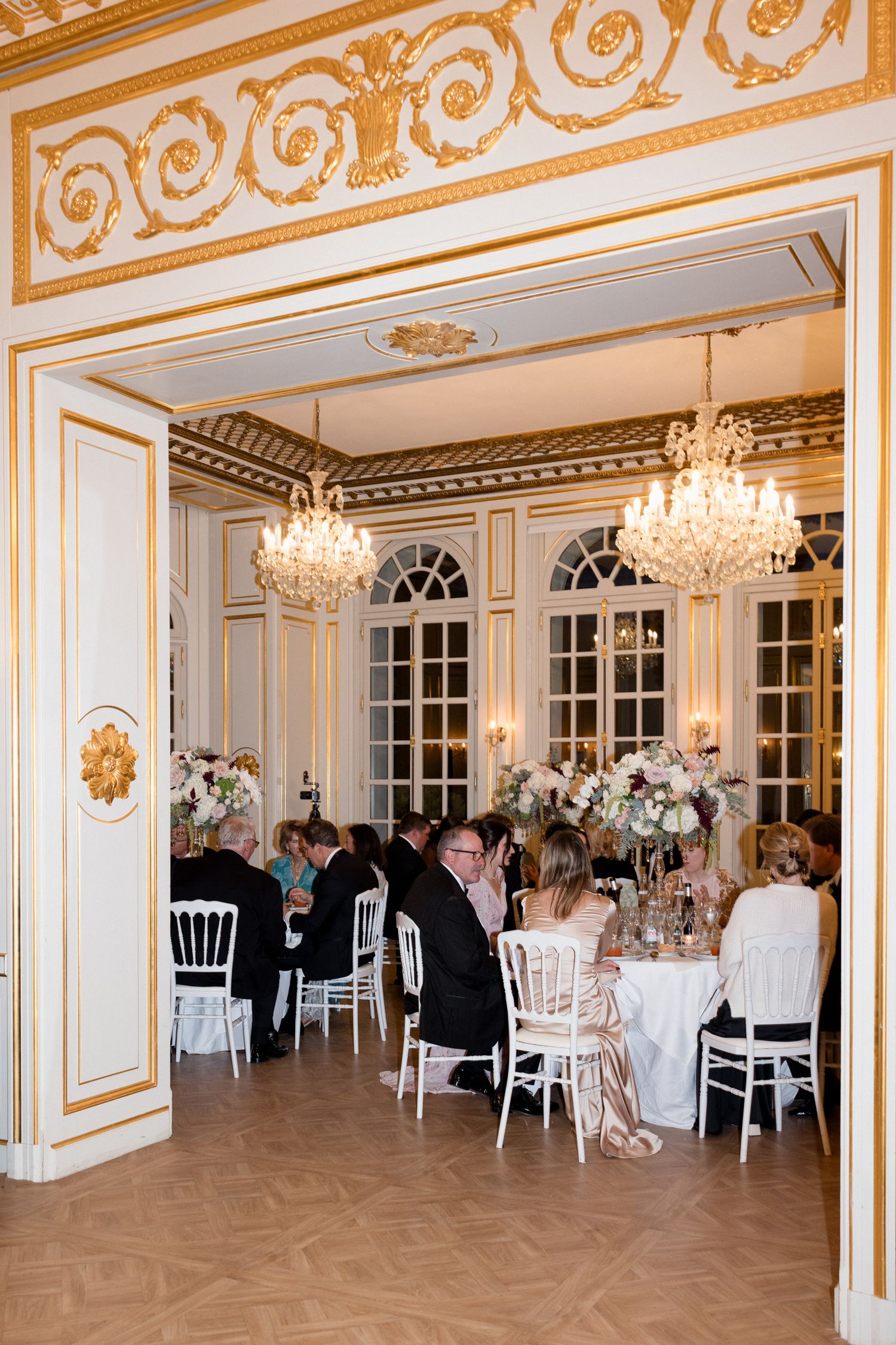 Elegant ballroom with ornate gold trim, crystal chandeliers, and round tables set for a formal wedding reception de bouche en bouche caterer