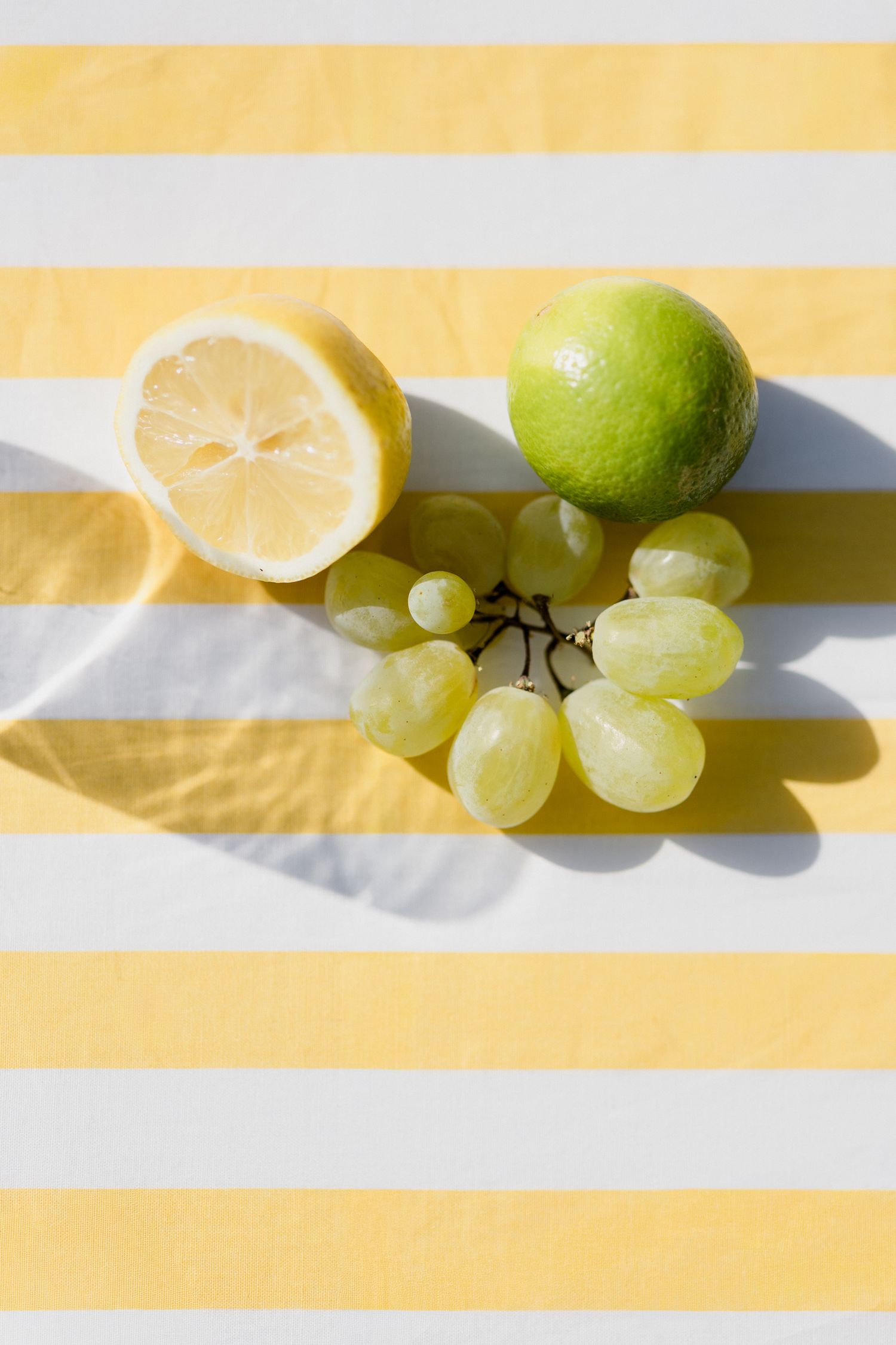 Fresh citrus fruits and green grapes arranged on a light colored surface with dramatic shadows.