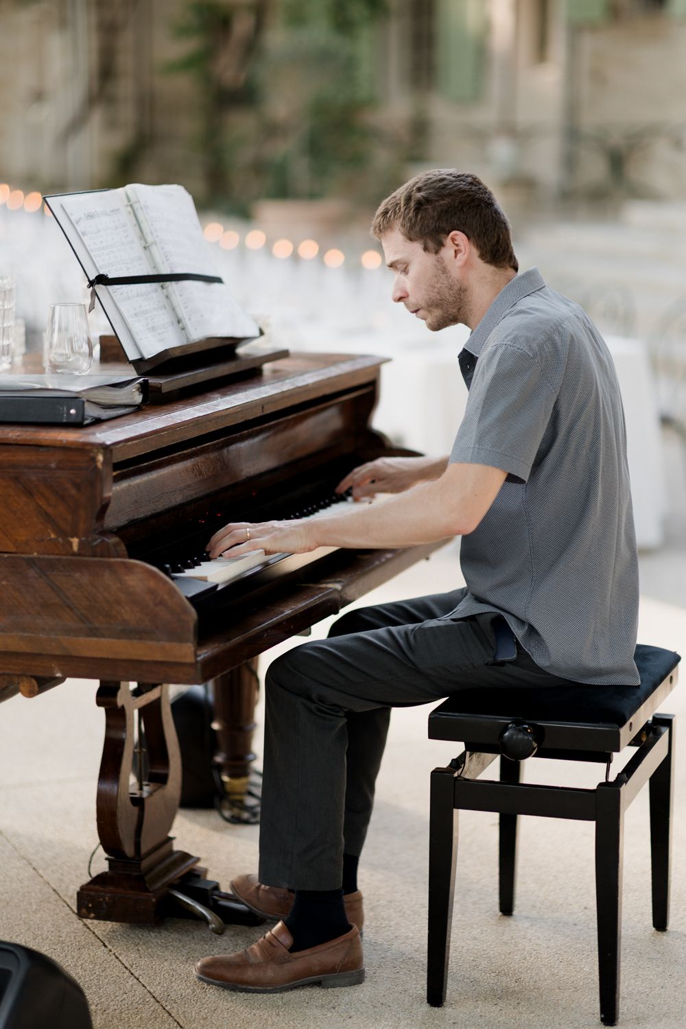 Pianist performs on a wooden grand piano in a softly lit space wearing casual attire. Julien Pianiste