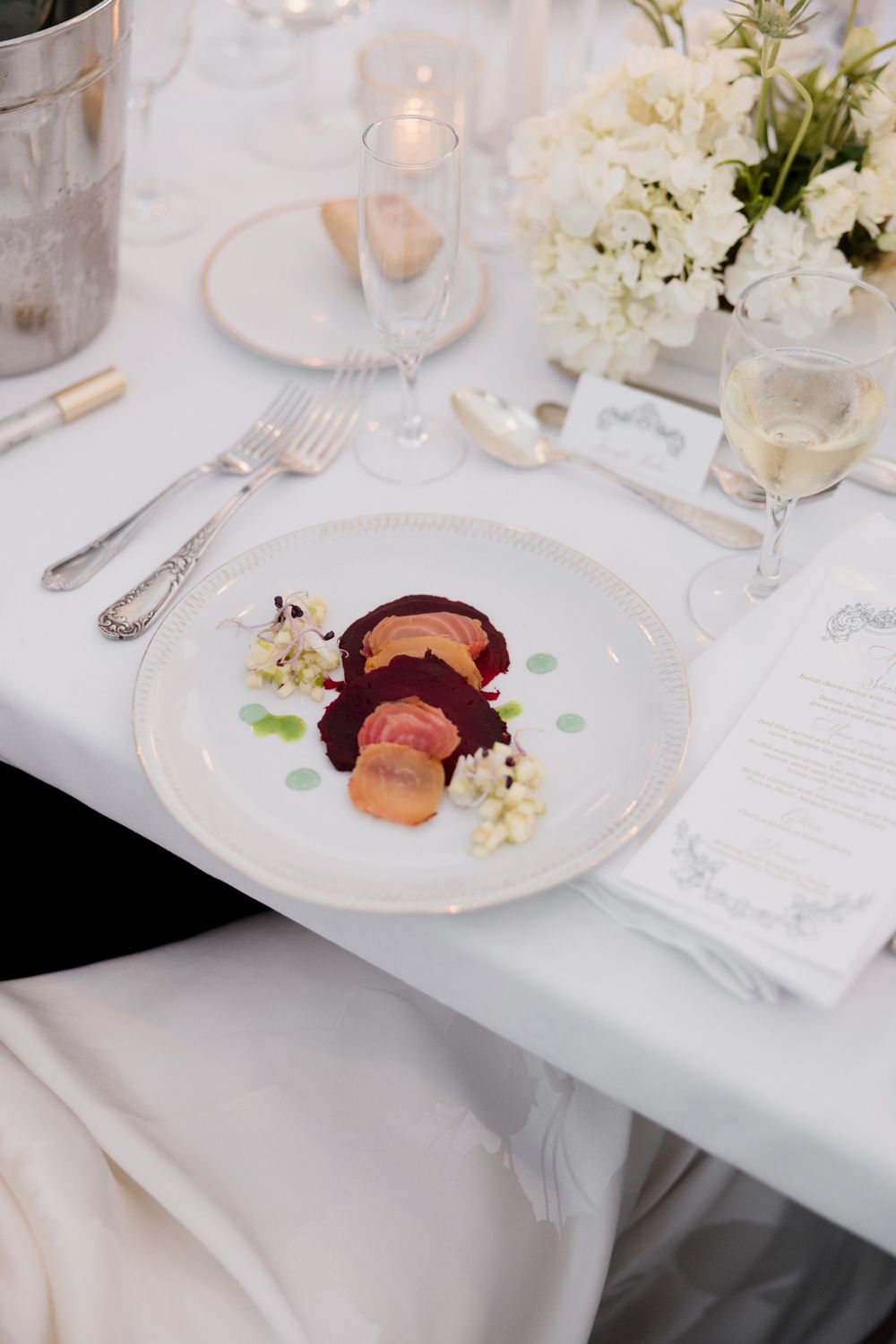 White table settings at an elegant wedding reception with floral centerpieces and burgundy accents. Mets d'ici traiteur