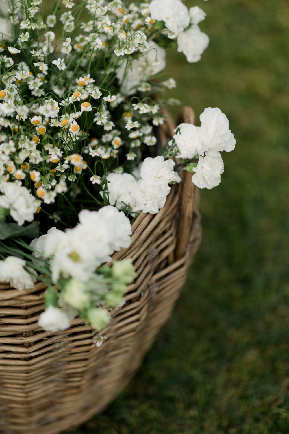 Delicate white flowers and daisies arranged in a rustic woven basket against green foliage.