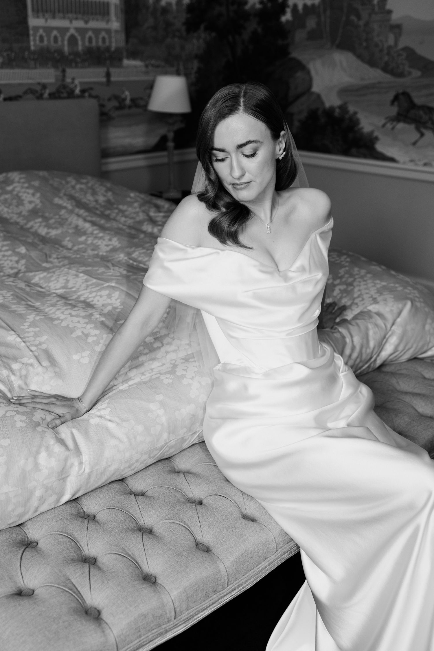 A person in a flowing white dress reclines gracefully on a tufted gray couch in black and white photography.