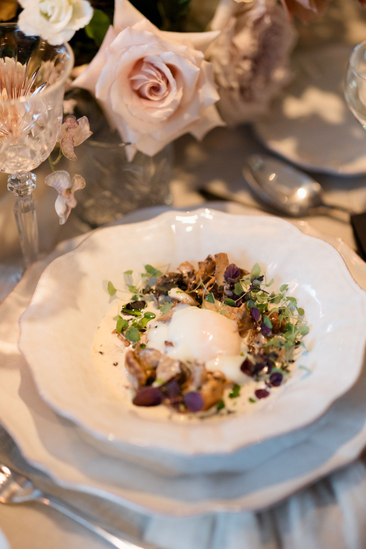 Elegant plated dishes garnished with microgreens and pink roses on white plates at an upscale dining event.