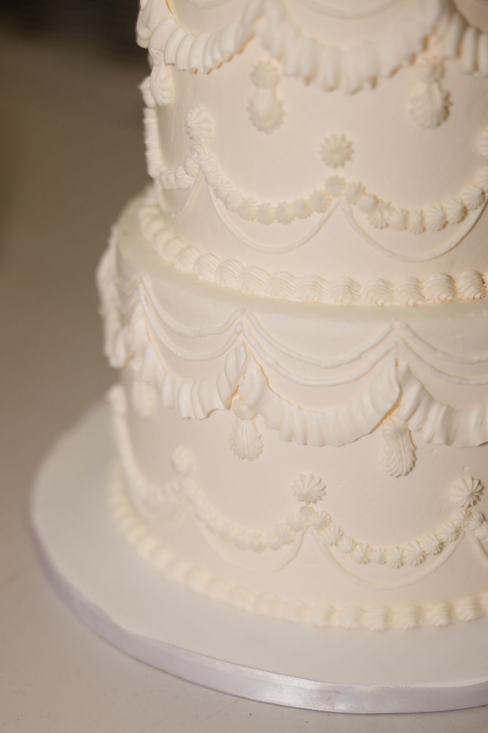 Close-up detail of an elegant white wedding cake with delicate piped scalloped design and traditional buttercream decoration.