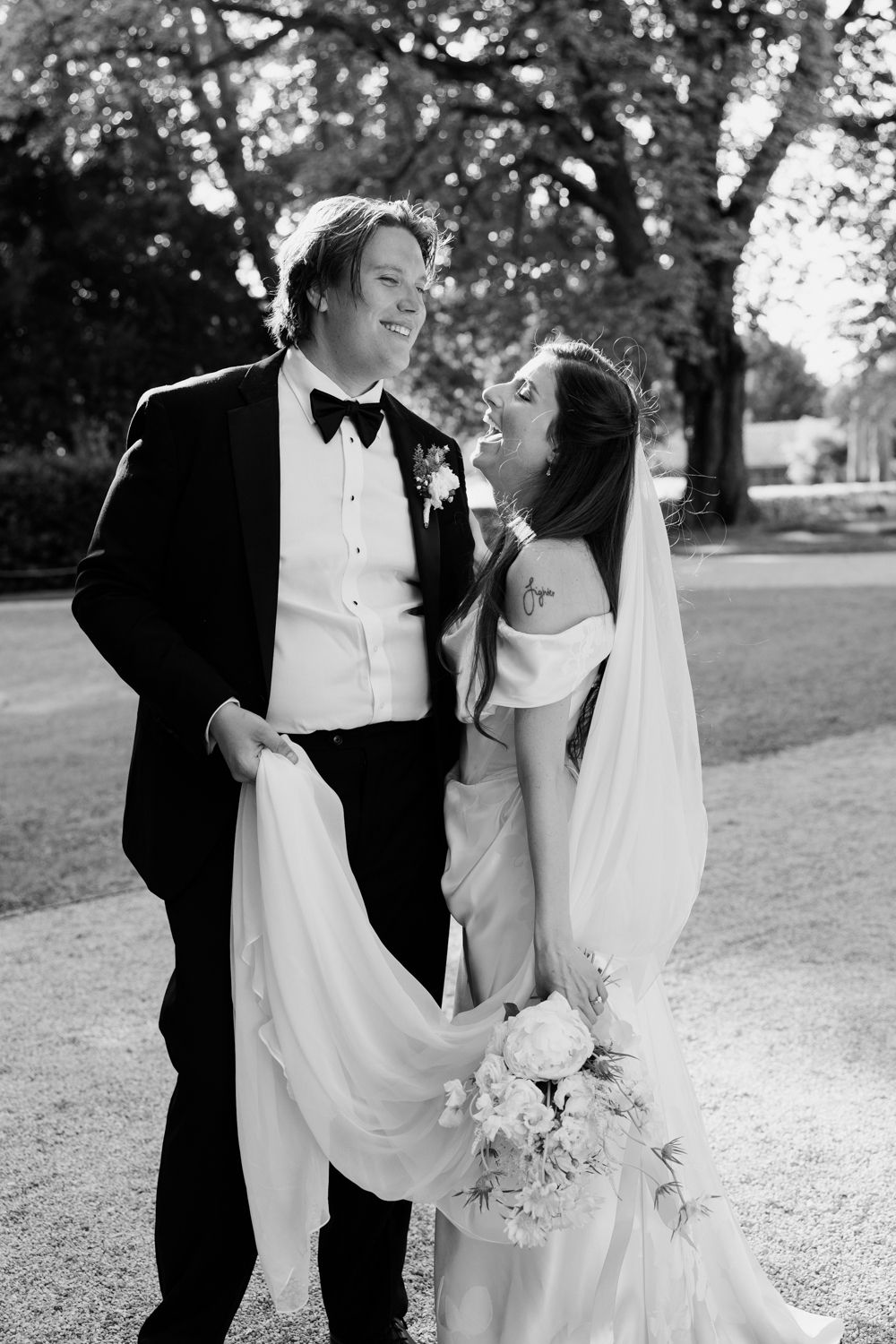 A bride and groom share a joyful moment outdoors on their wedding day in black and white photography.
