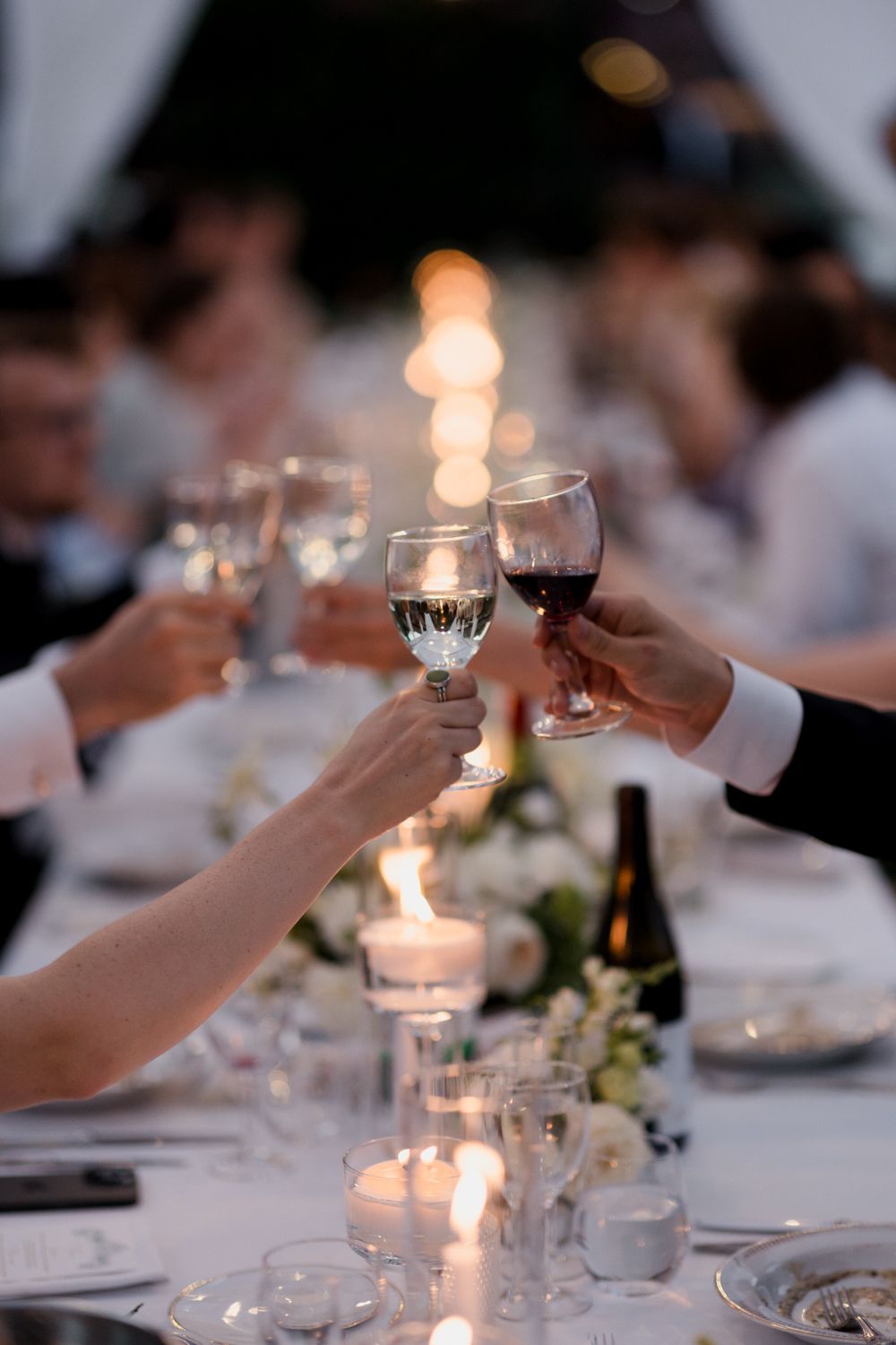 Candlelit table settings at an elegant dinner party with wine glasses being raised in a celebratory toast.