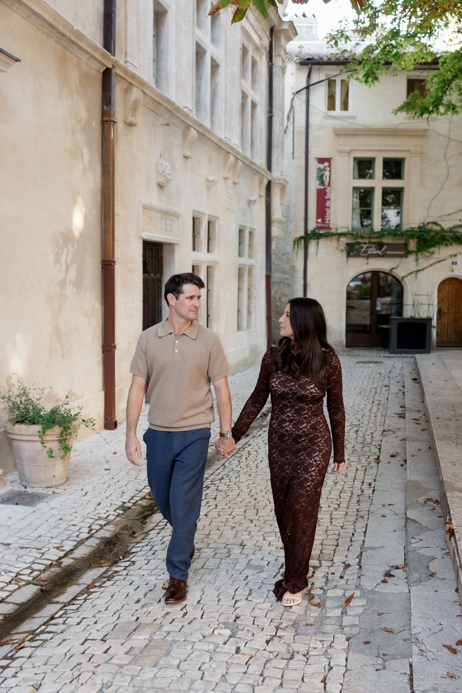 A couple walks hand in hand along a charming cobblestone street in a historic European city neighborhood.