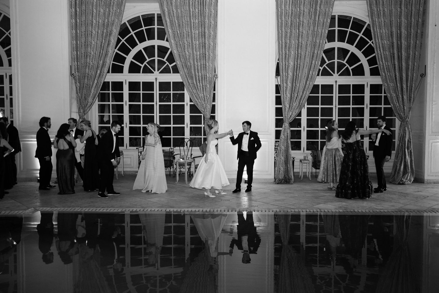 Black and white photo series showing wedding reception moments in an elegant ballroom with arched windows and drapes. Editorial wedding