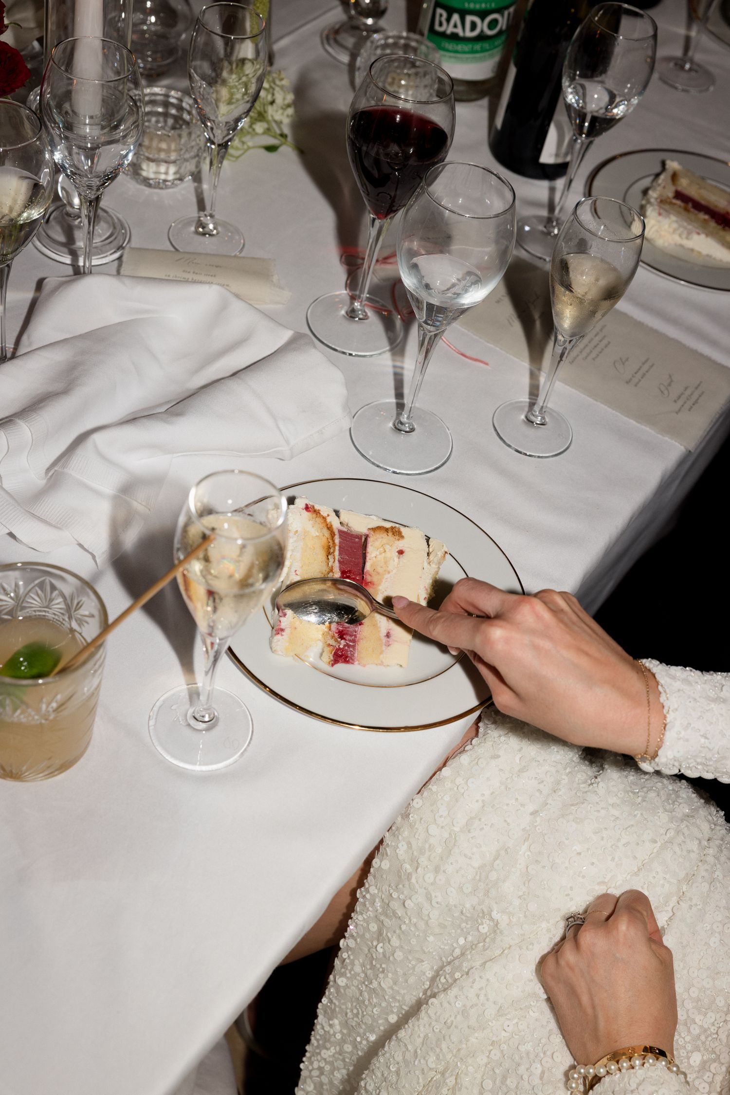 Hands holding wine glasses and plates on a white tablecloth at an elegant dining setting. Photographe mariage france luxe