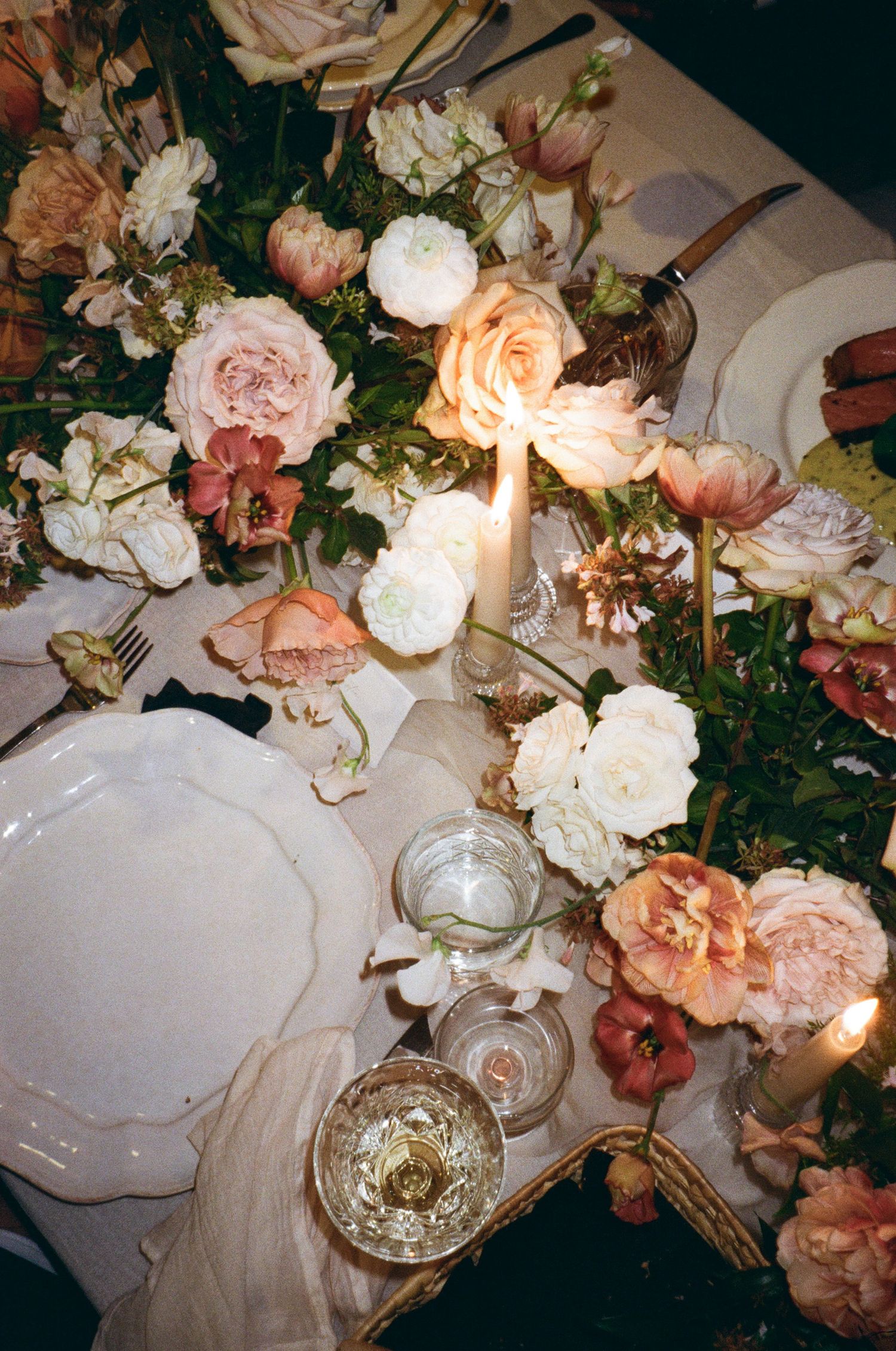 Elegant table setting with soft peach and white roses, candlelight, and delicate glassware creating a romantic ambiance.