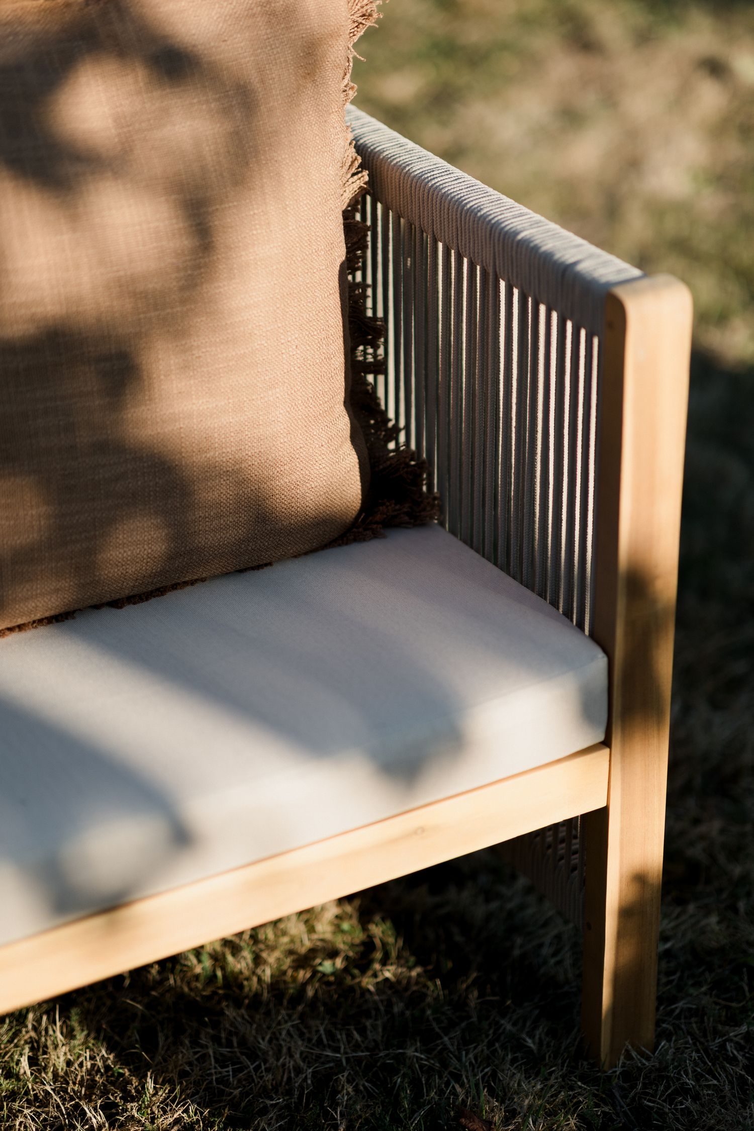 Wooden bench with white cushioning casting dramatic shadows on grass in evening sunlight.