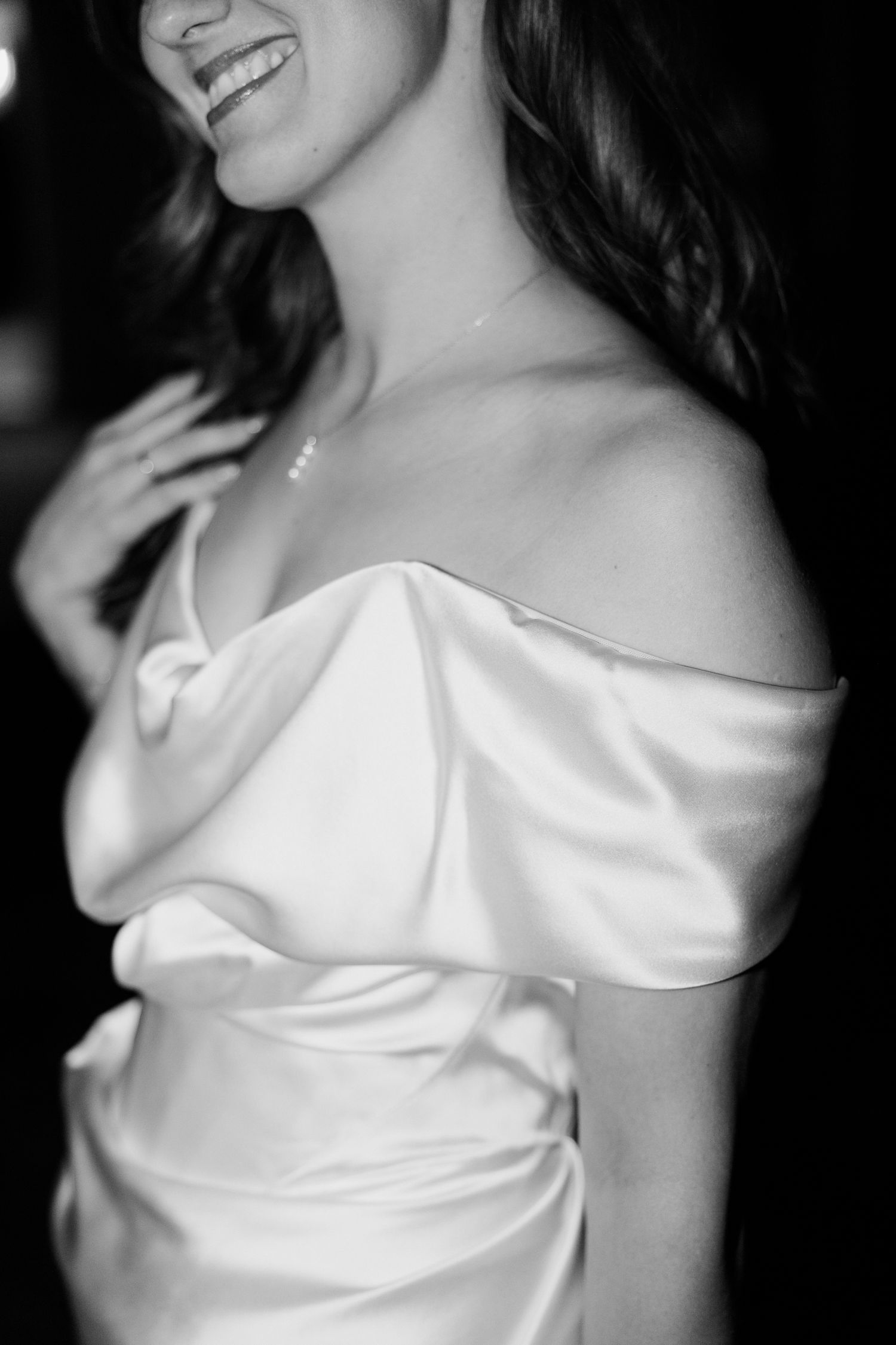 Black and white close-up of a bride in an off-shoulder white satin dress showing a joyful smile.