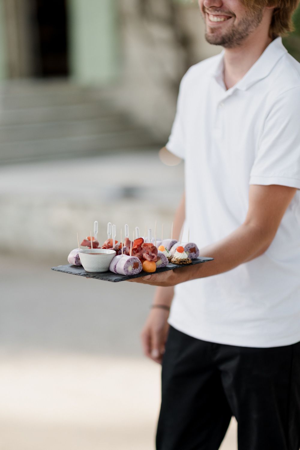A person in a white shirt carries a tray of artfully plated desserts at a restaurant service.