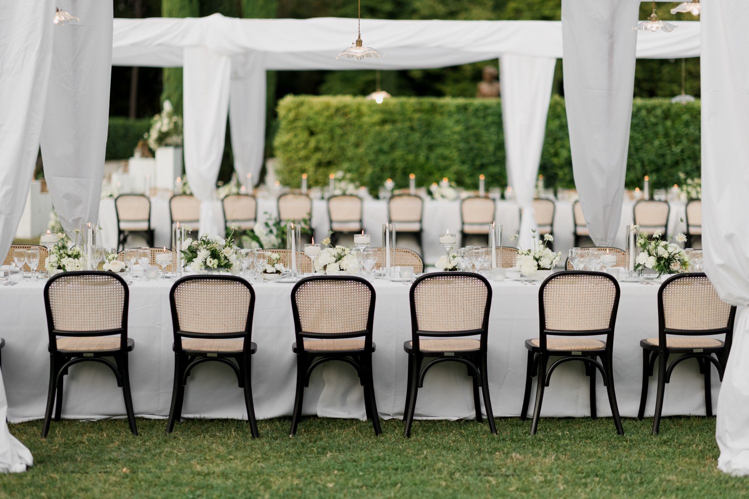 Elegant outdoor wedding reception setup with white fabric draping and rows of formal dining tables.