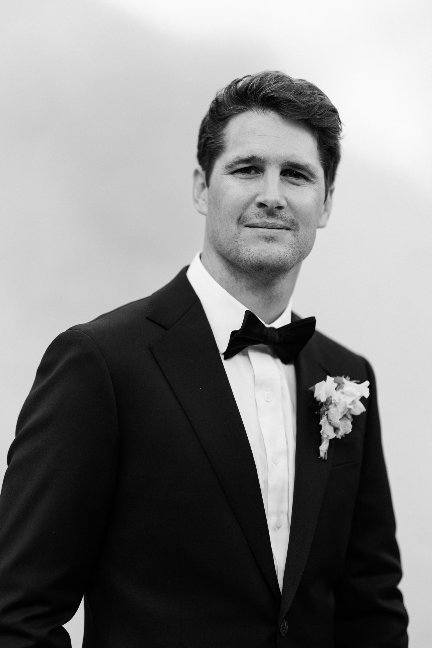 Black and white portrait series of a groom in a classic tuxedo and bow tie with boutonniere. wedding photographer france