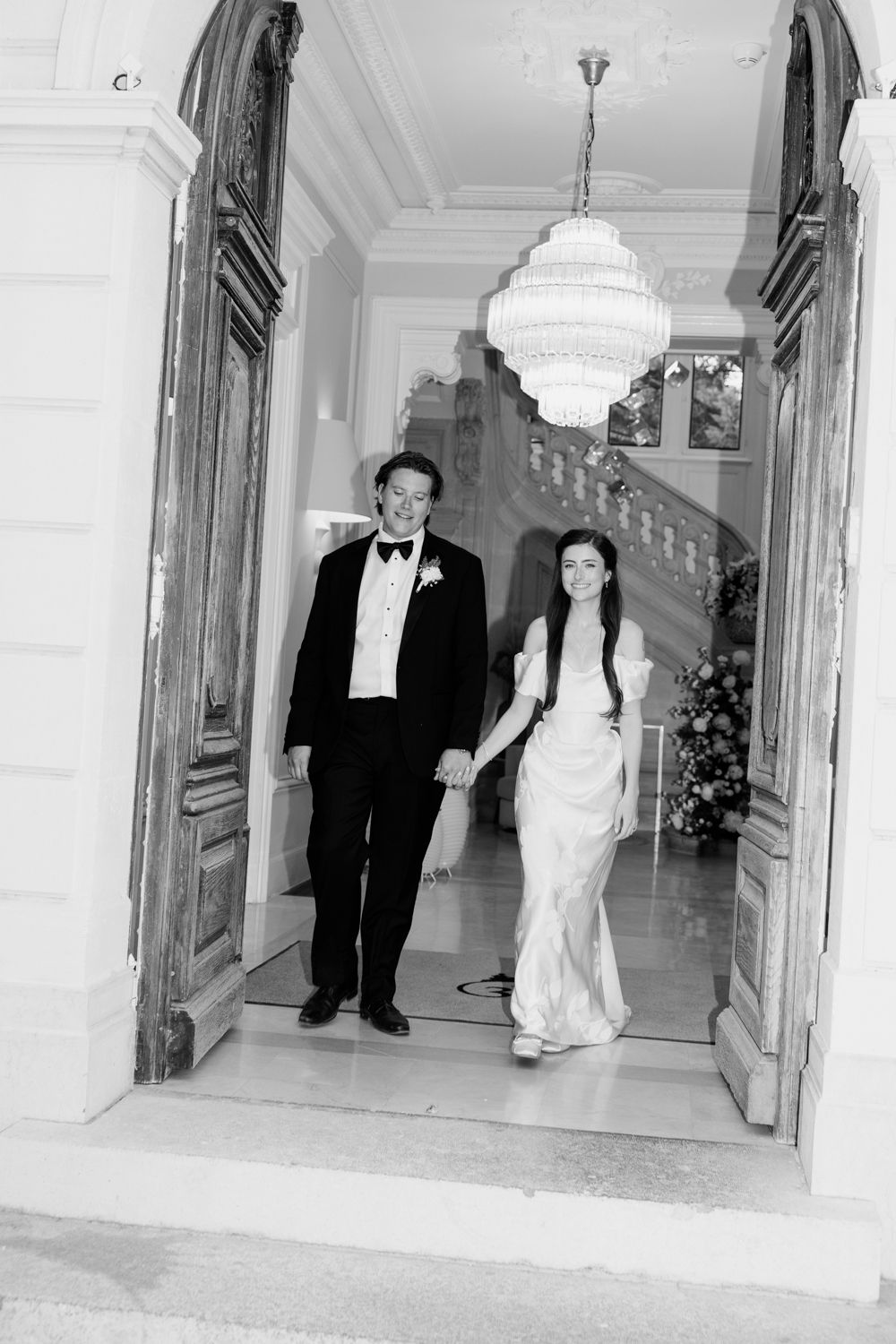 Formal black and white wedding photos showing a couple walking down an elegant hallway with ornate decor and columns.