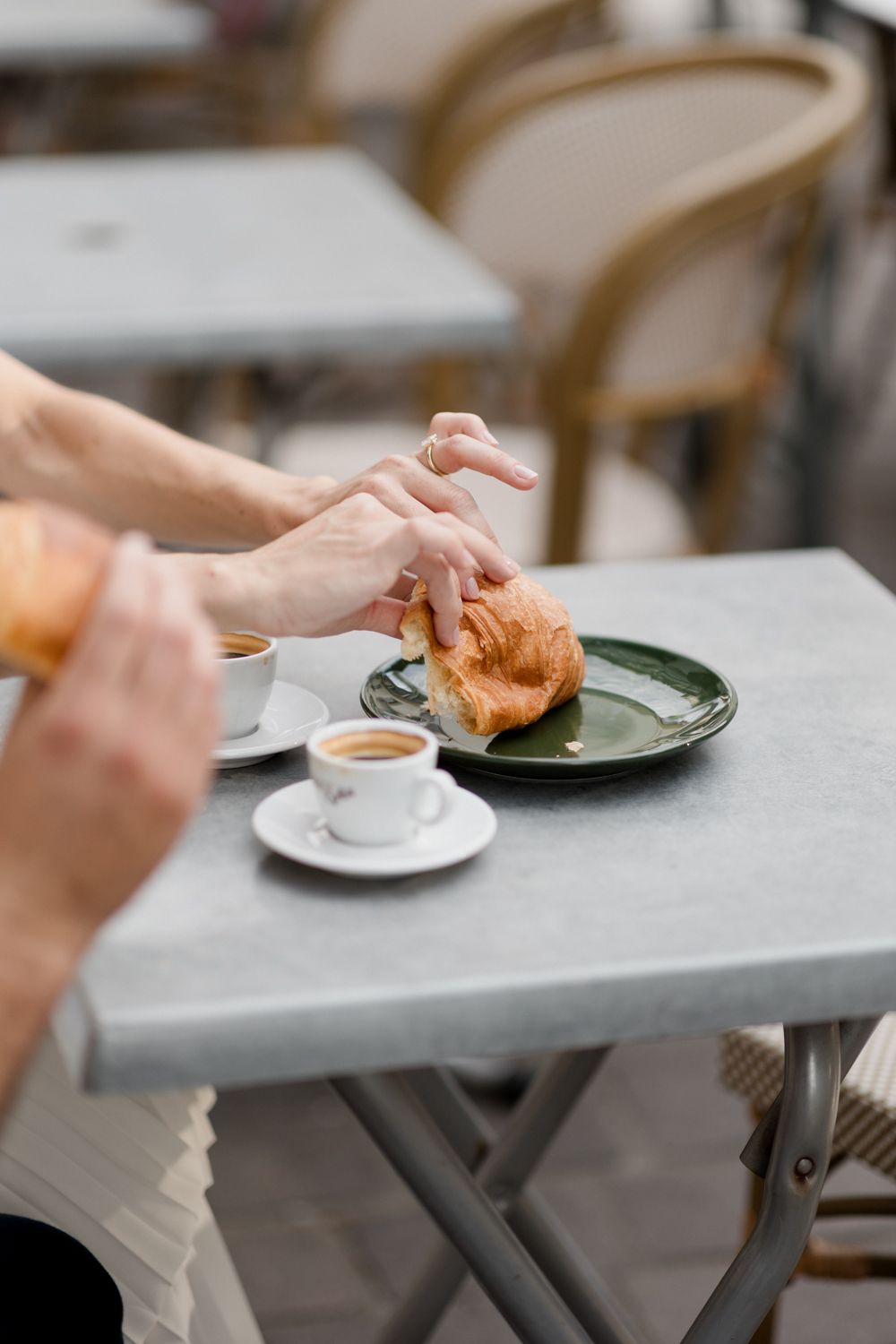 A series of hands reaching across a gray tabletop to grab pastries from plates in a cafe setting.