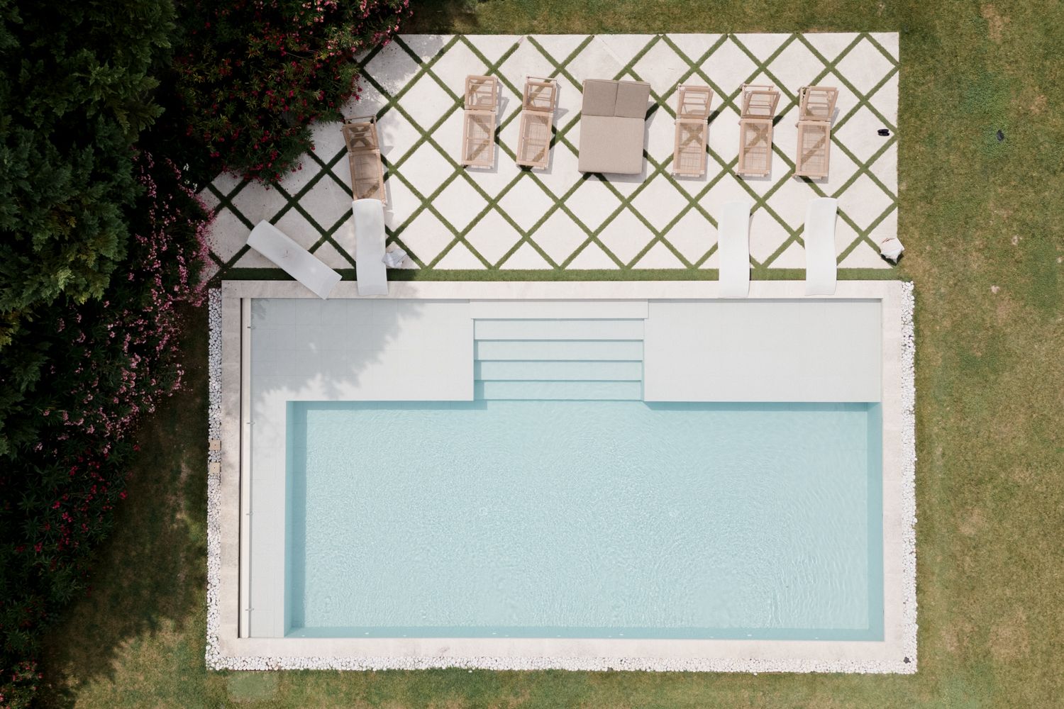 Aerial view of a rectangular swimming pool with teal water and white patio featuring a lattice pergola structure. Château des 3 Fontaines