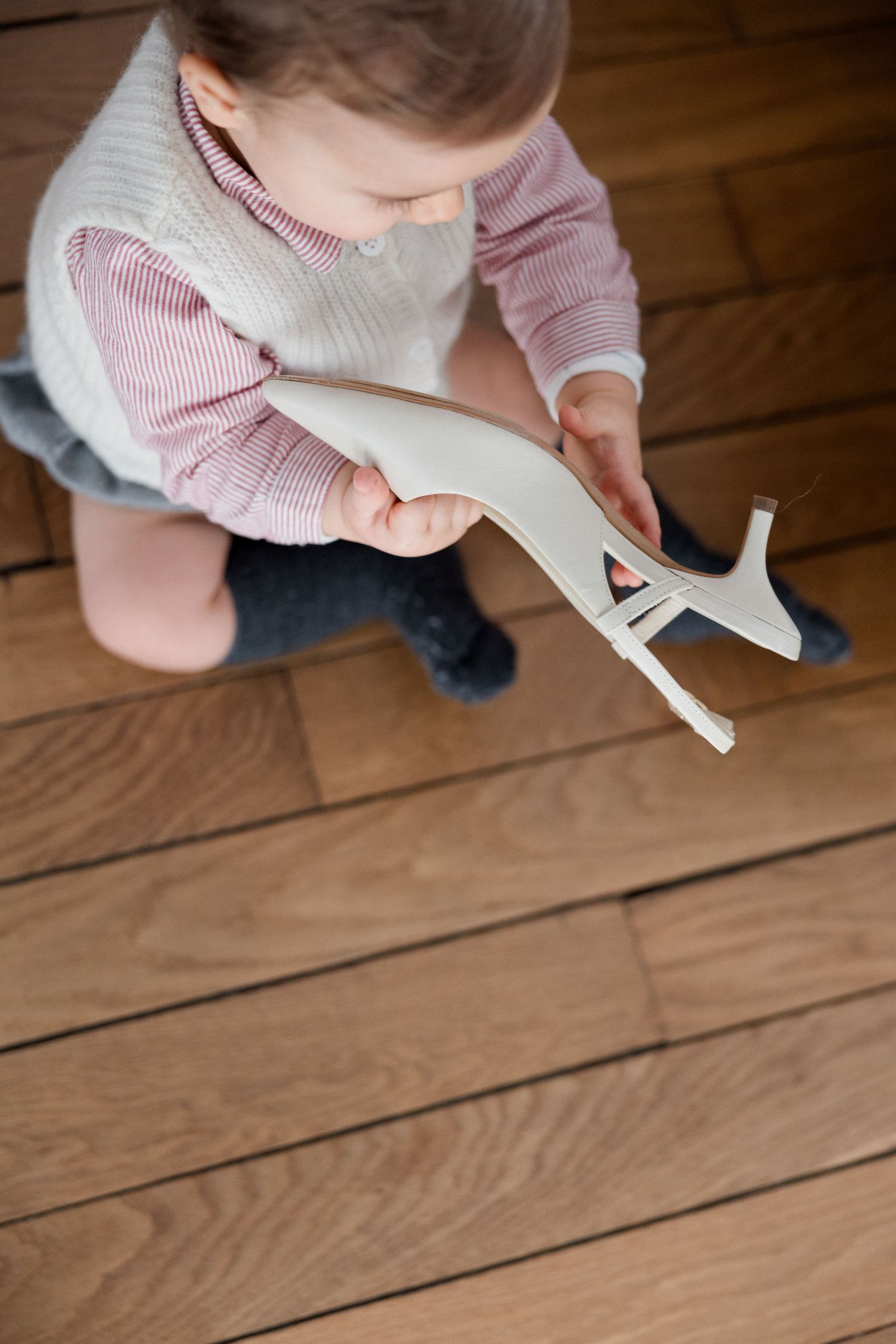 A toddler sits on hardwood floor, holding and examining a wooden toy animal figure.