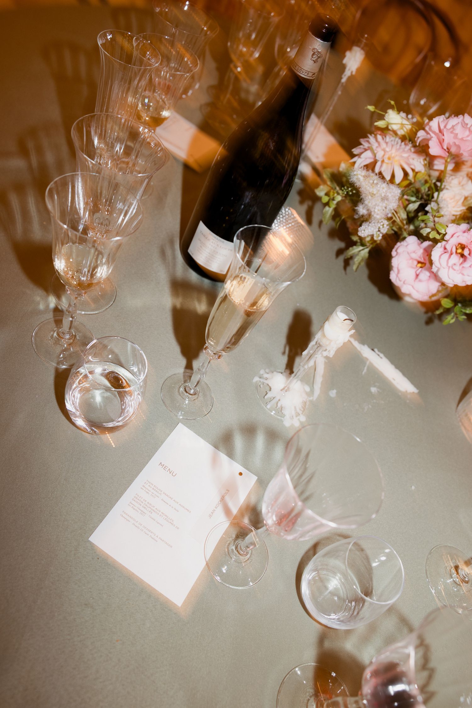 Elegant wine glasses and pink floral arrangements on a reflective surface create a romantic dining atmosphere.