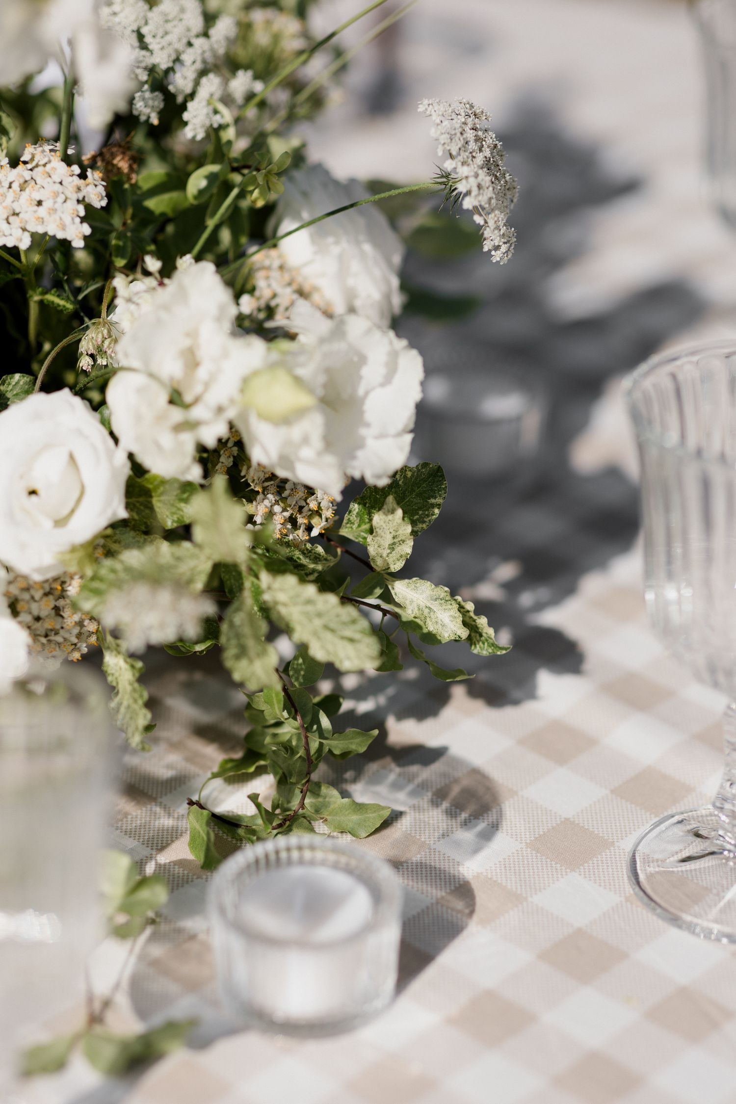 White floral centerpiece arrangements with delicate blooms on a checkered tablecloth at an elegant event setting.