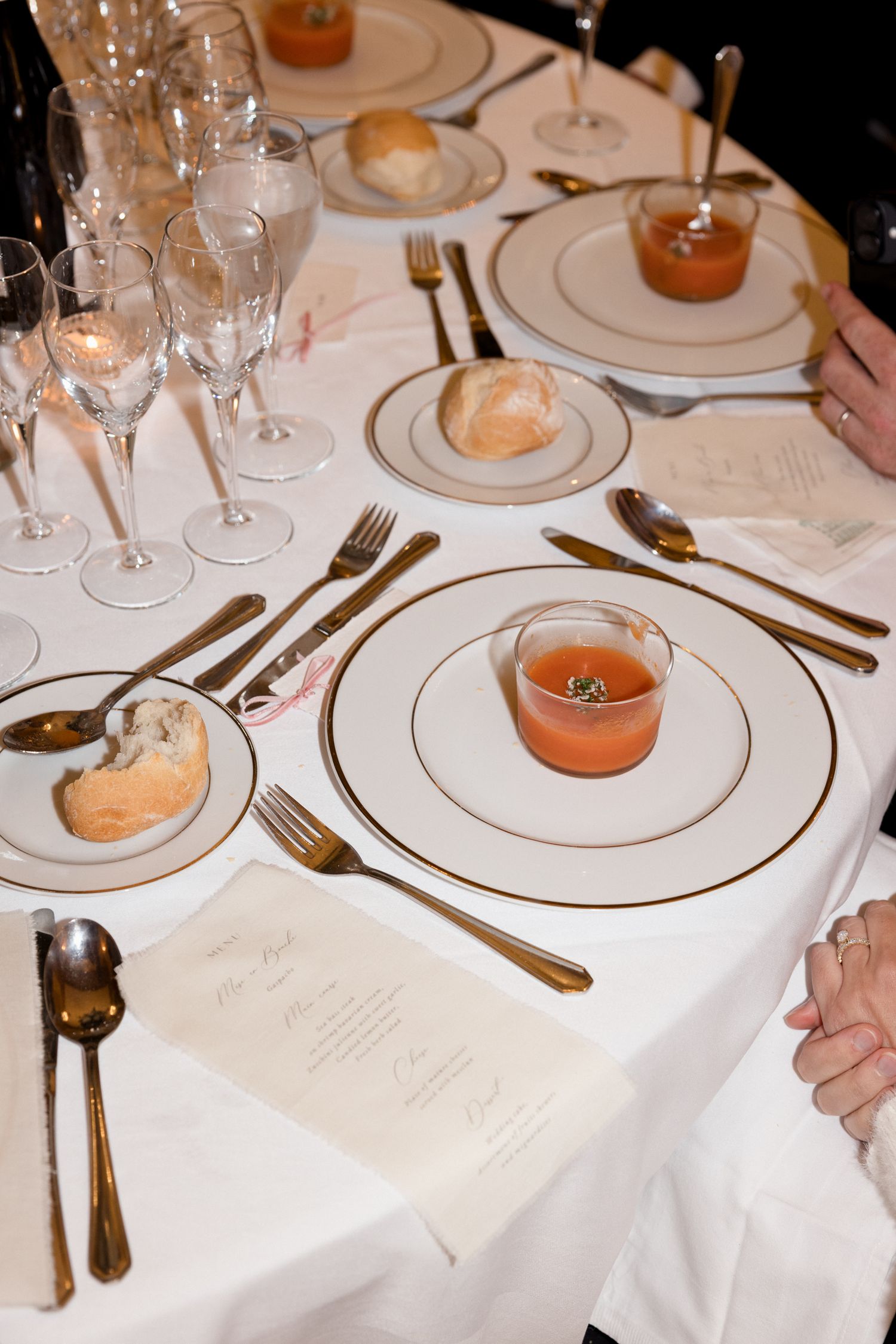 Elegant table settings with white linens, wine glasses, and amber-colored drinks in small glasses on formal place settings