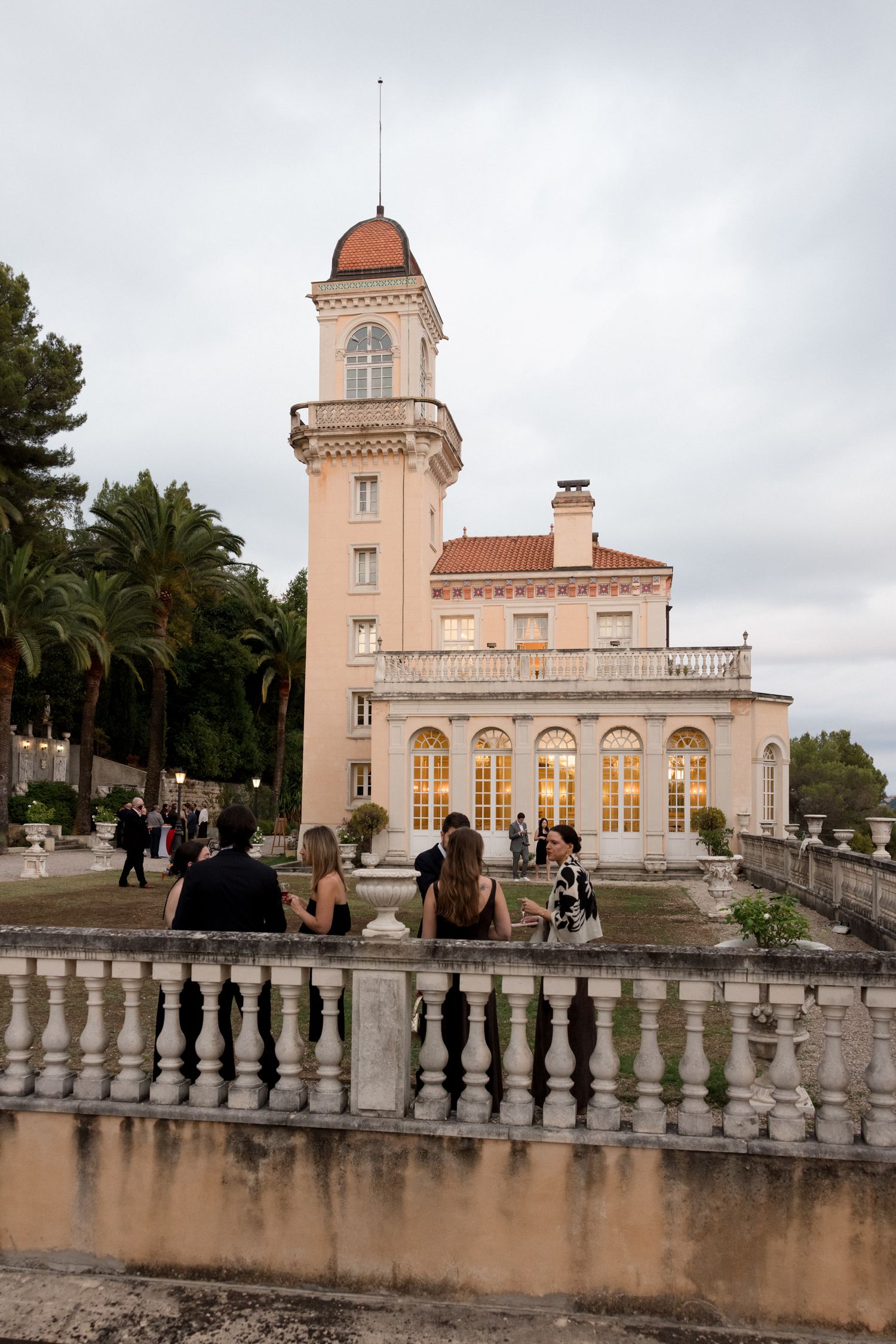Historic pink villa with tower and arched windows overlooking balustrade terrace with palm trees in Mediterranean setting. chateau grasse