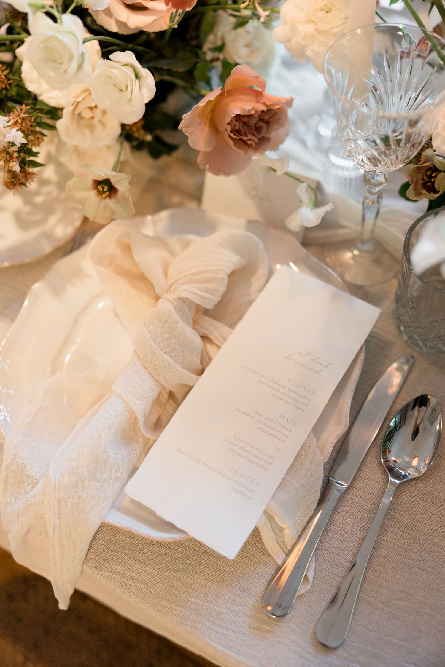 Elegant table setting with white floral arrangements, menu cards, and crystal glassware on a light gray tablecloth.