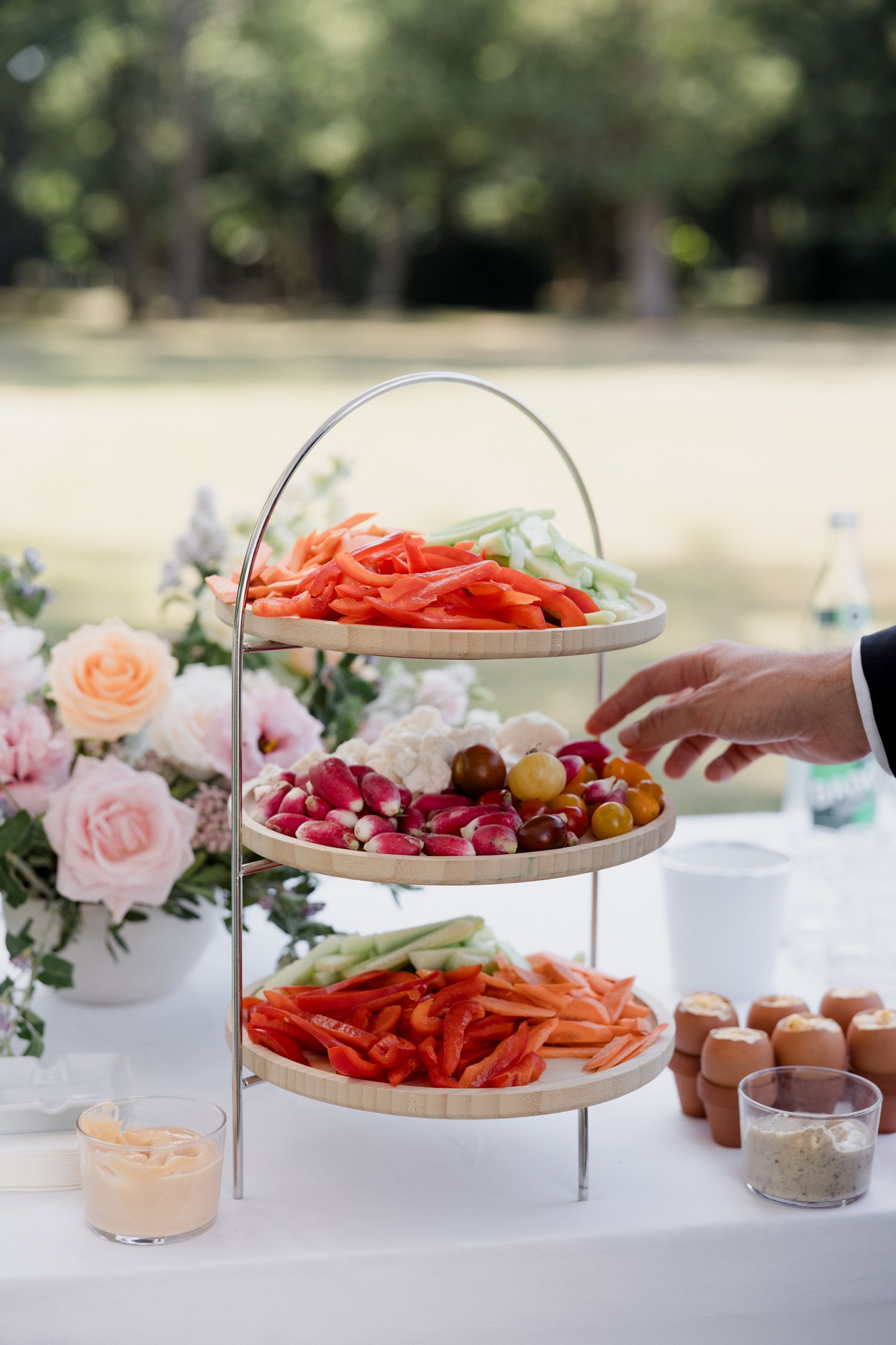 Elegant party buffet setup with tiered serving platters displaying colorful vegetables, eggs and appetizers on a white tablecloth.