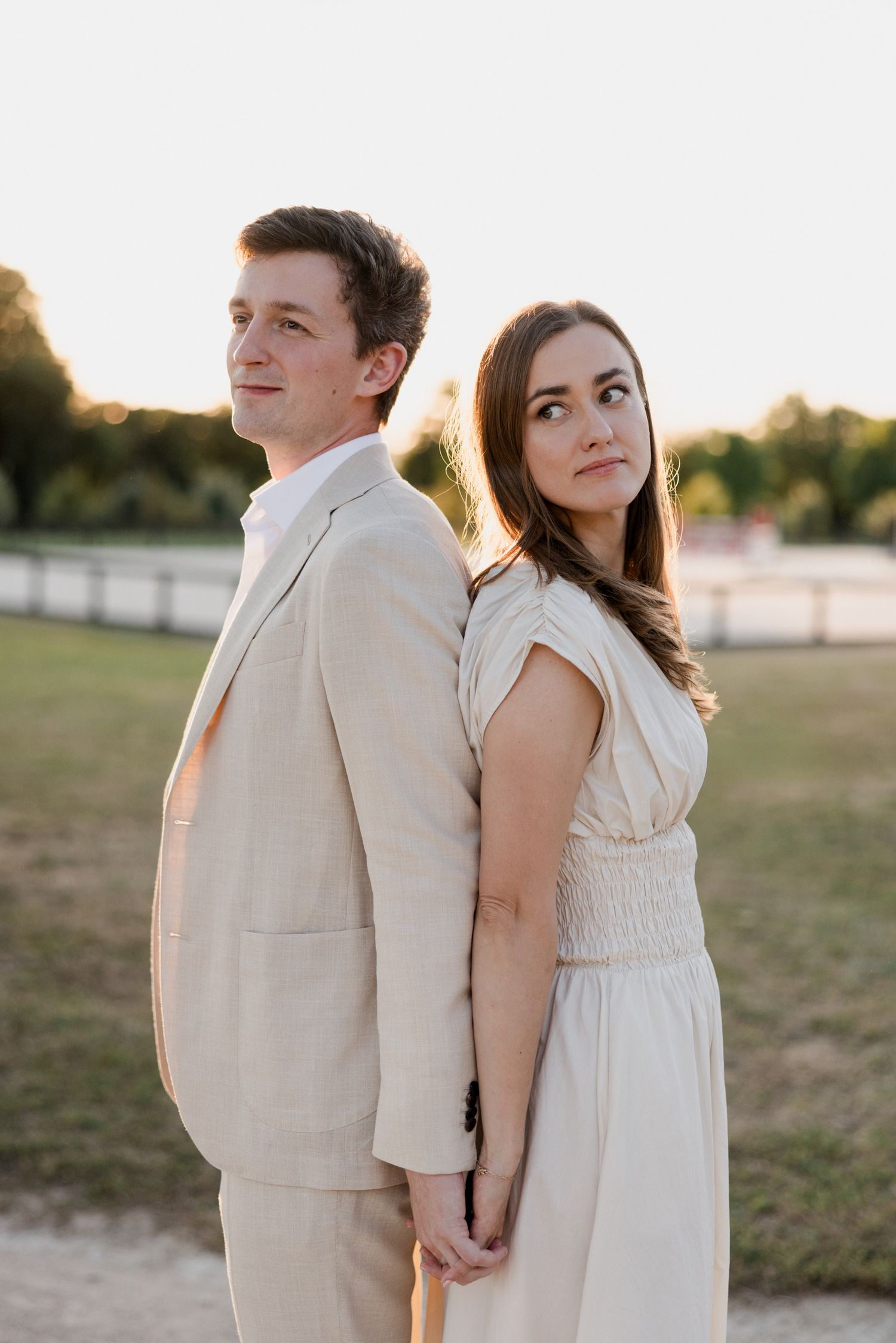 A couple in white outfits holding hands while standing back to back in a grassy field at sunset. Photographe mariage Tours