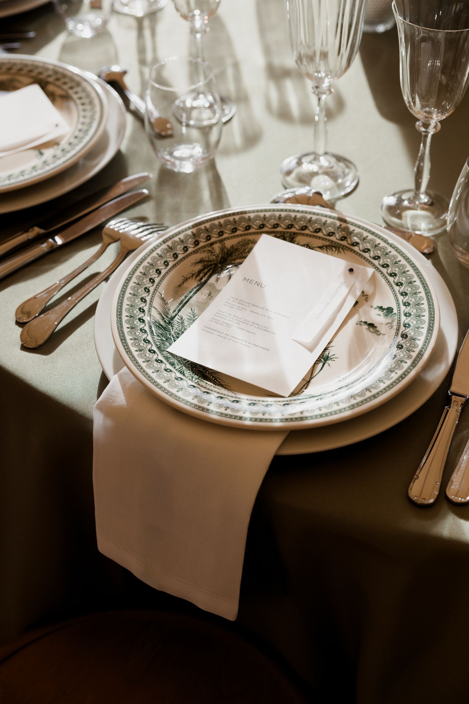 Elegant place settings at a formal dining table with white plates, napkins and wine glasses in soft lighting. Luxury wedding france