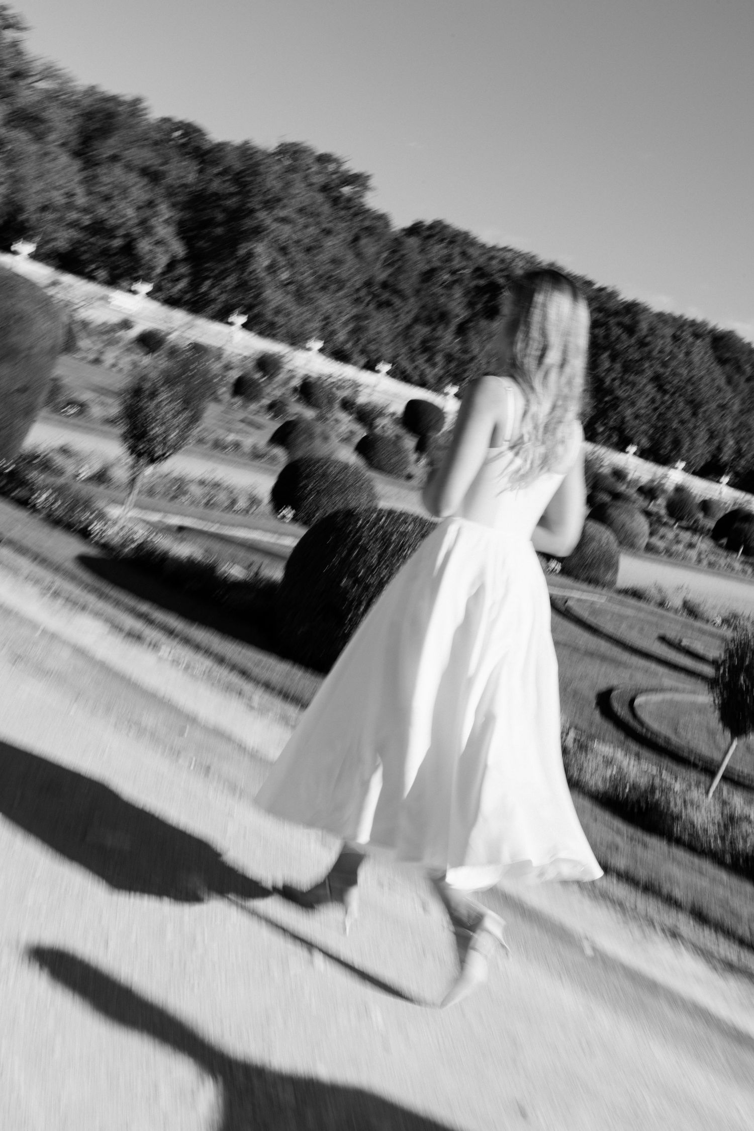 Black and white motion blur photo of bride in white gown walking through formal French garden.