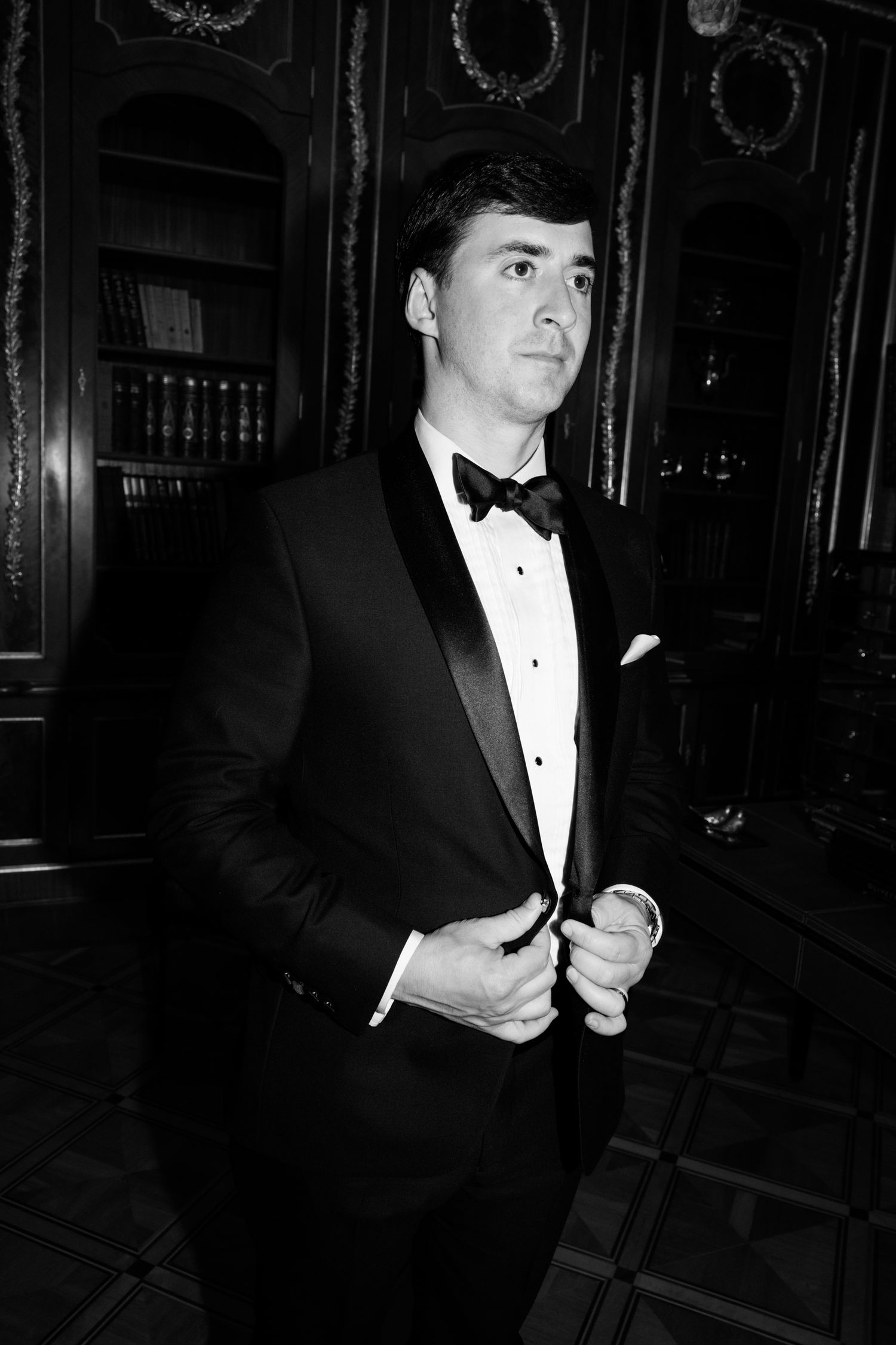 A black and white photo series showing someone in a tuxedo adjusting their bowtie in an elegant interior setting.