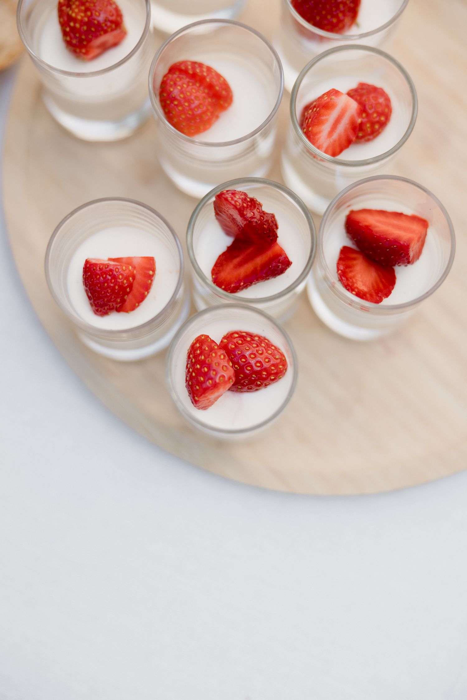 Small glass cups filled with creamy white dessert topped with fresh sliced strawberries arranged on a round serving plate. Pool party loire