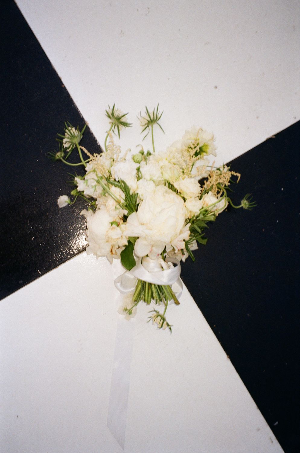 White floral bouquet with delicate green foliage on a black and white background creates a striking contrast. Wedding film photography
