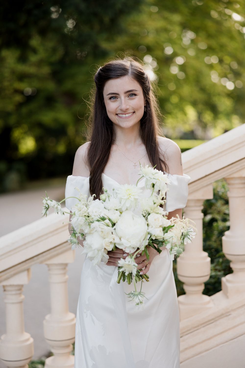 A wedding portrait series showing a bride in white holding an elegant white floral bouquet on marble steps in natural light.