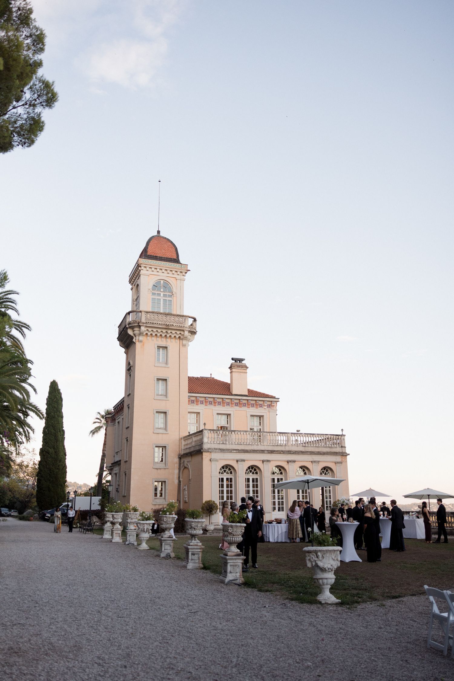 Elegant Mediterranean-style villa with tower and outdoor event gathering at dusk with decorative urns lining the path. Chateau saint georges