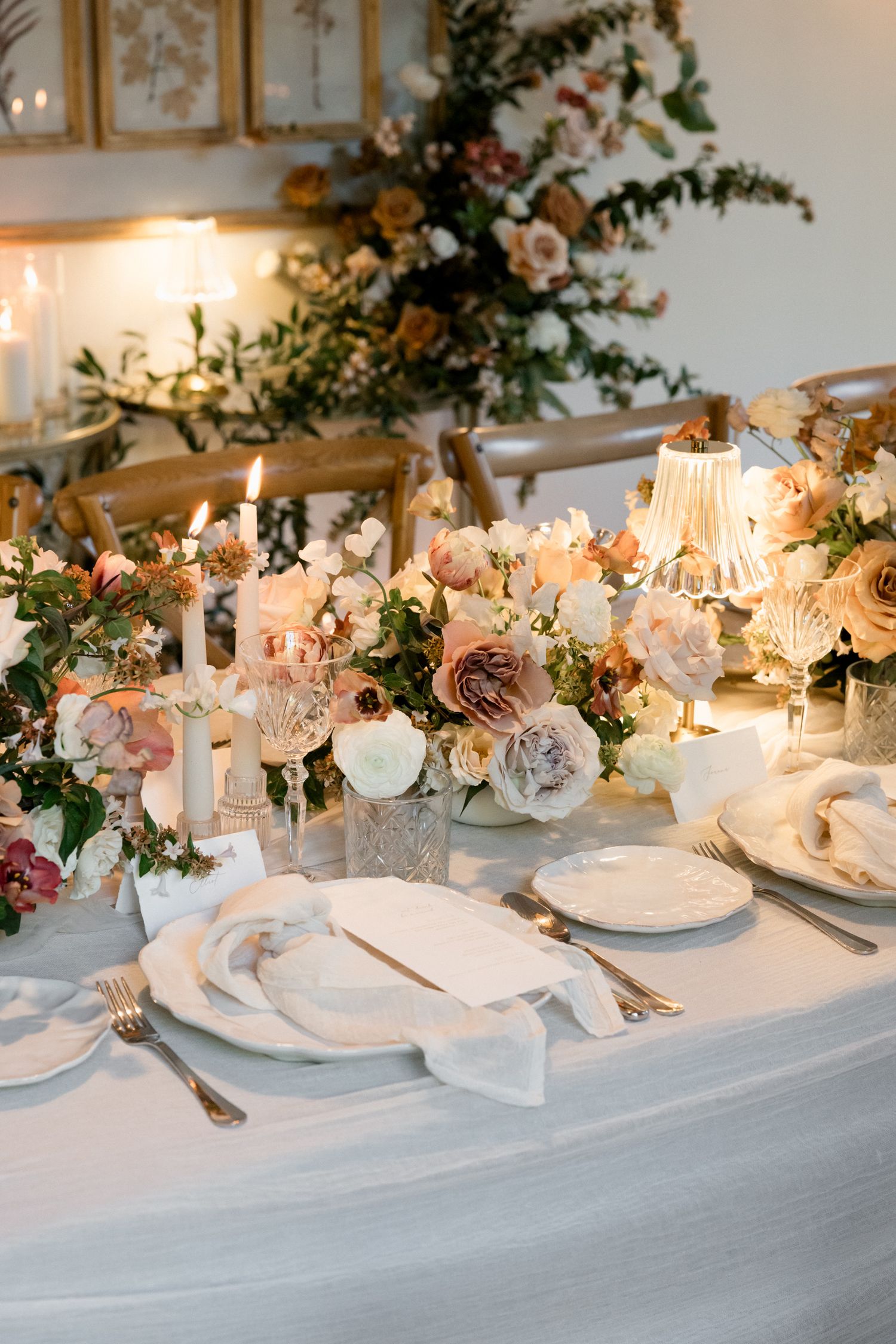 Close-up of romantic table setting with white linens, candlelight, and blush pink floral arrangements.