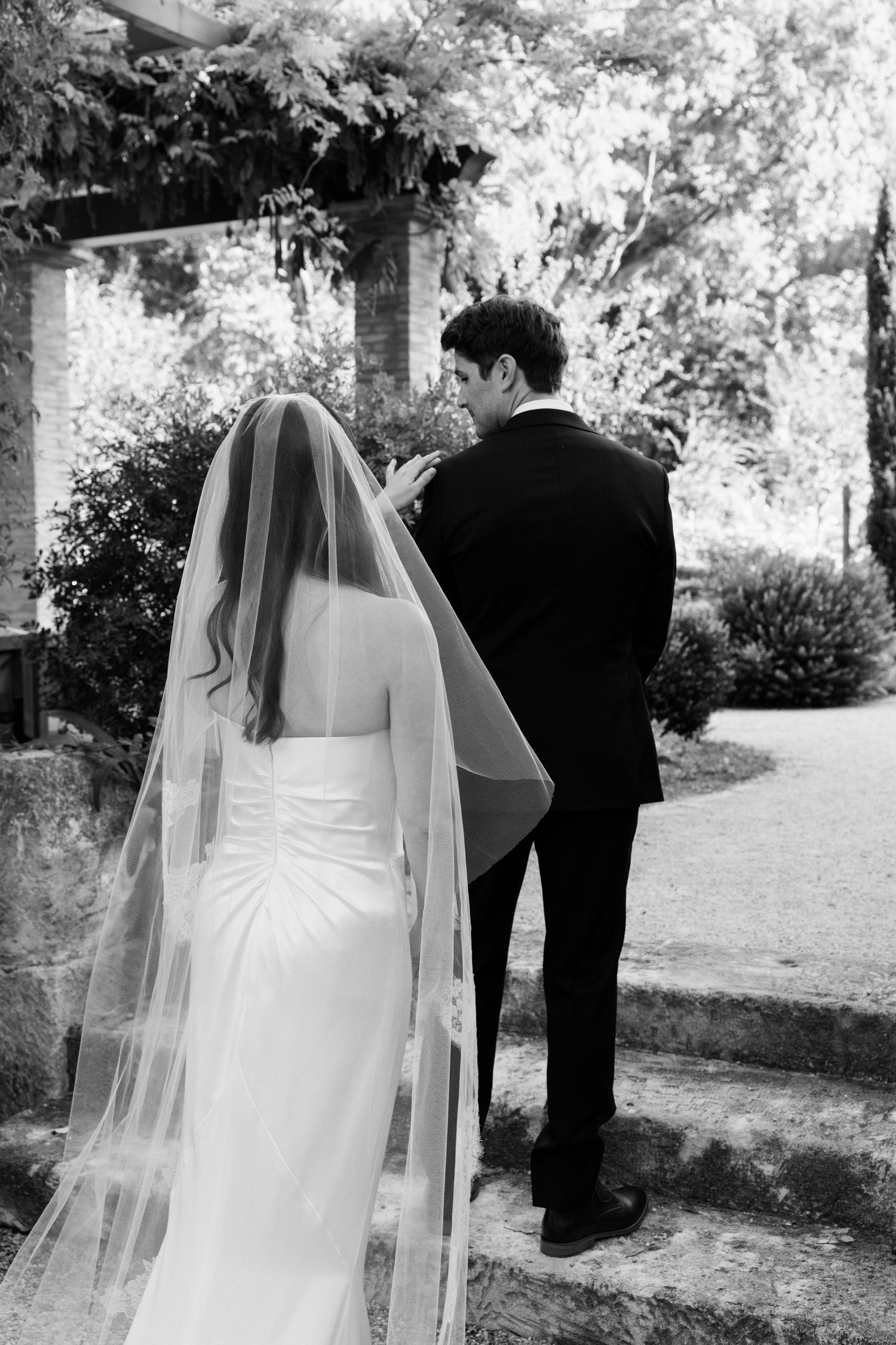 A bride and groom share an intimate moment in a garden setting captured in black and white.