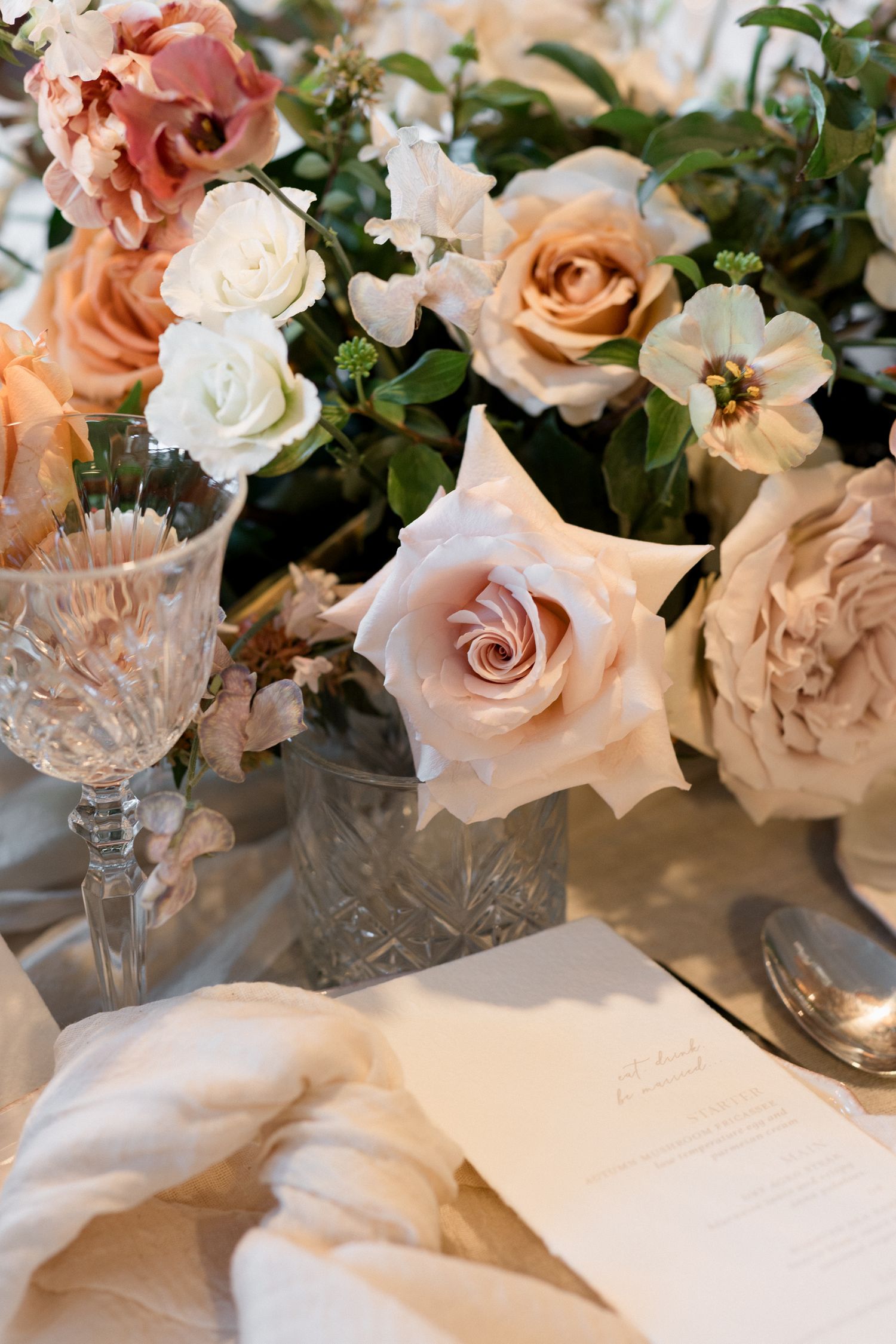 Elegant floral arrangement with peach and white roses alongside crystal glassware on a table setting. wedding photographer france