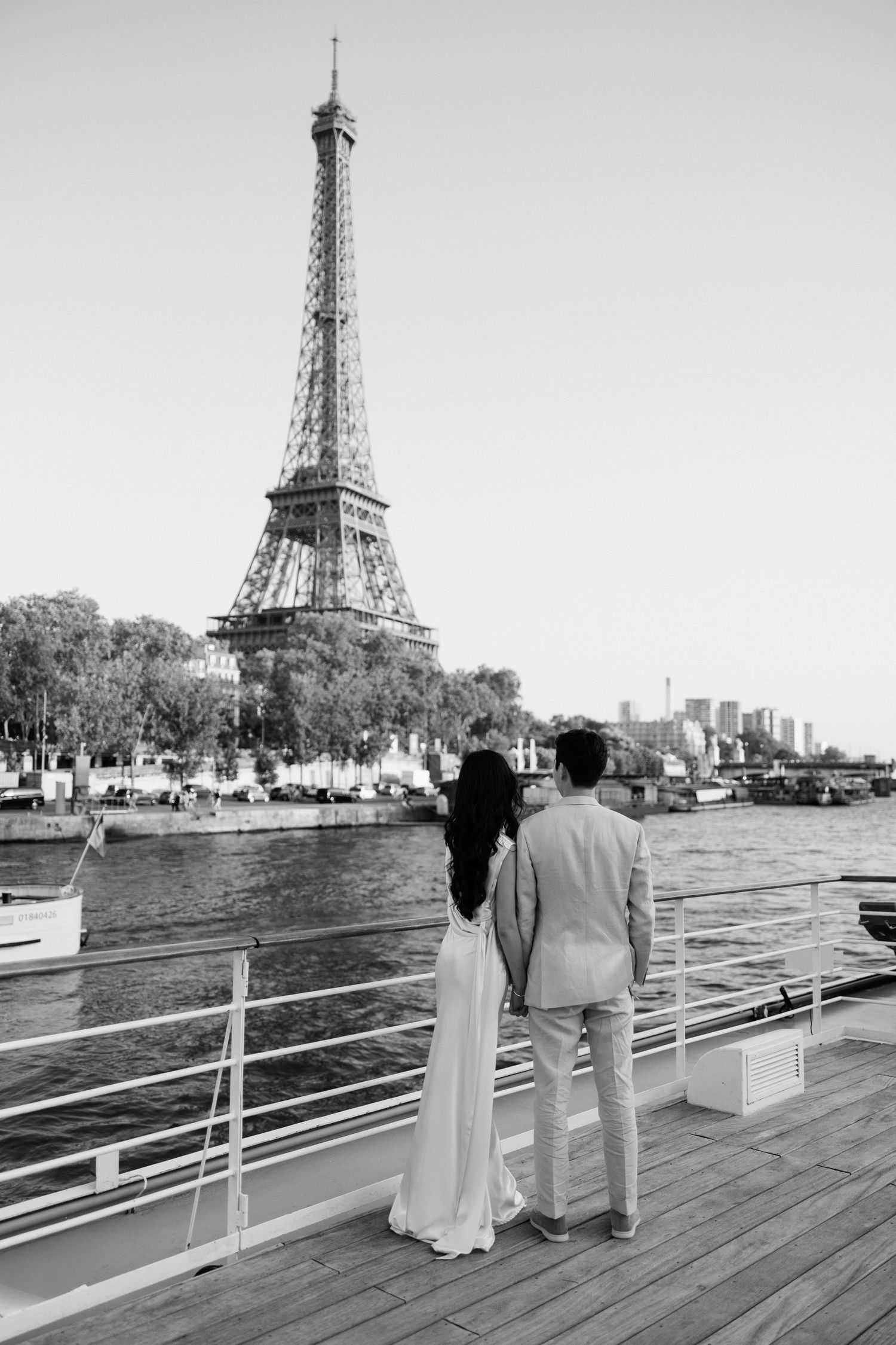 Couple holding hands on a boat deck gazing at the Eiffel Tower across the Seine River in Paris, black and white photo.